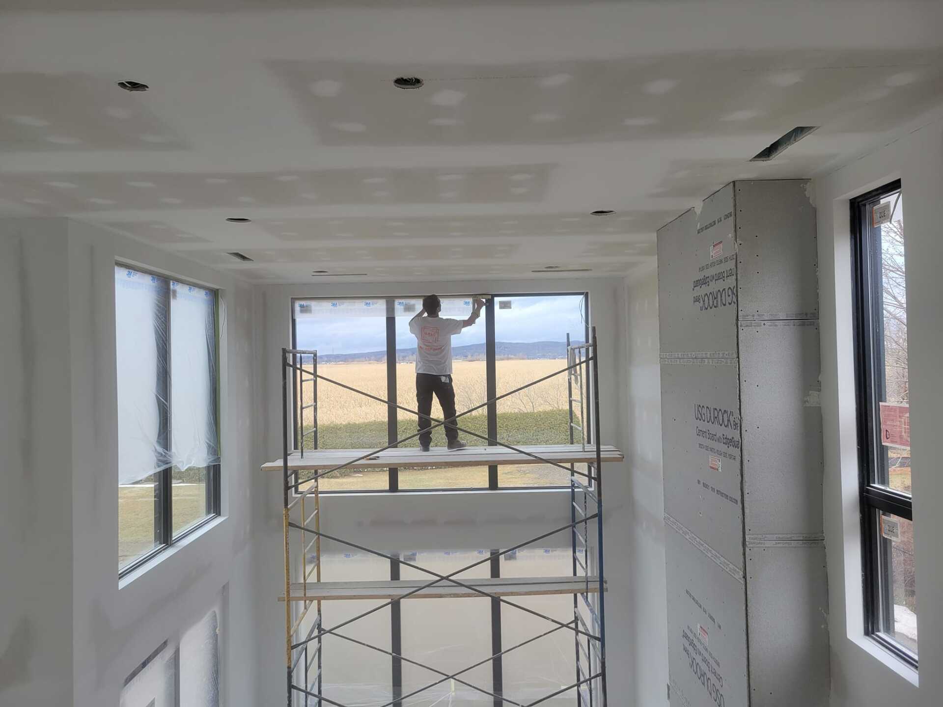 Un homme se tient debout sur un échafaudage dans une pièce avec beaucoup de fenêtres.