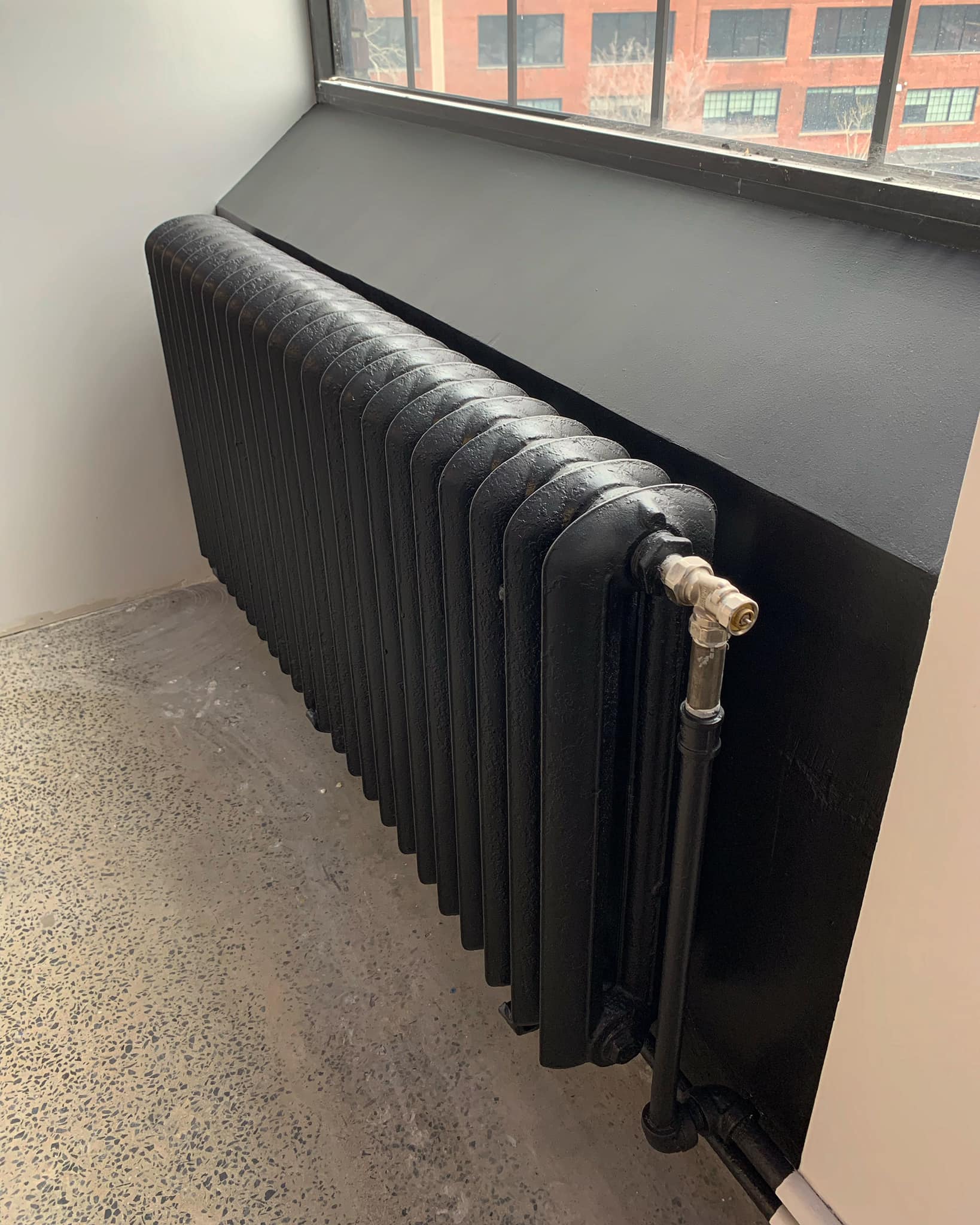 Un radiateur noir est posé à côté d'une fenêtre dans une pièce.