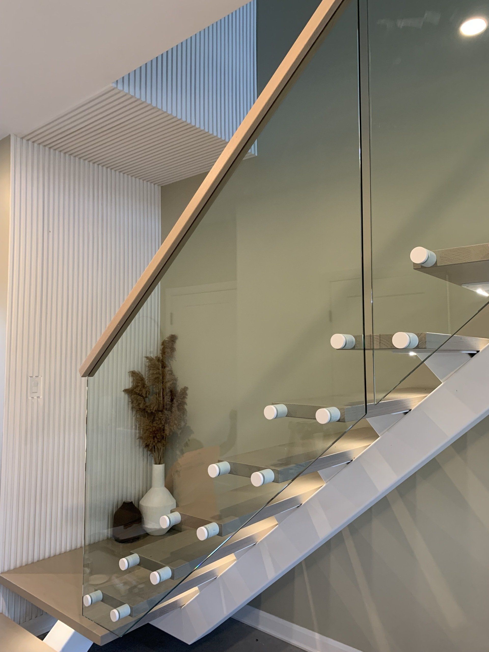 Un escalier moderne avec une rampe en verre et une main courante en bois.