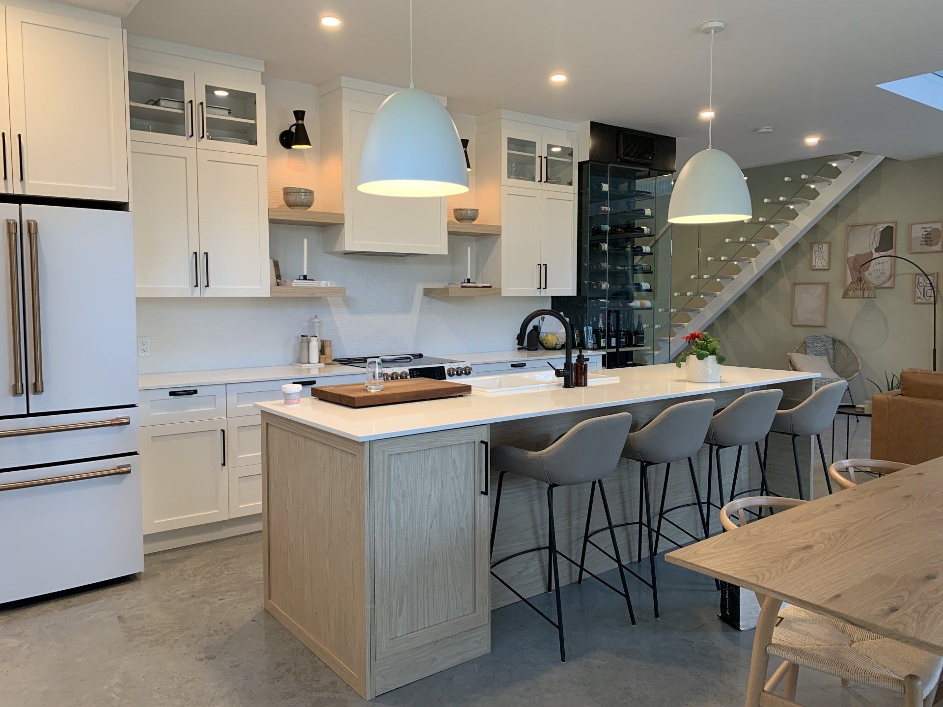 Une cuisine avec des armoires blanches, un grand îlot, des tabourets et une table.