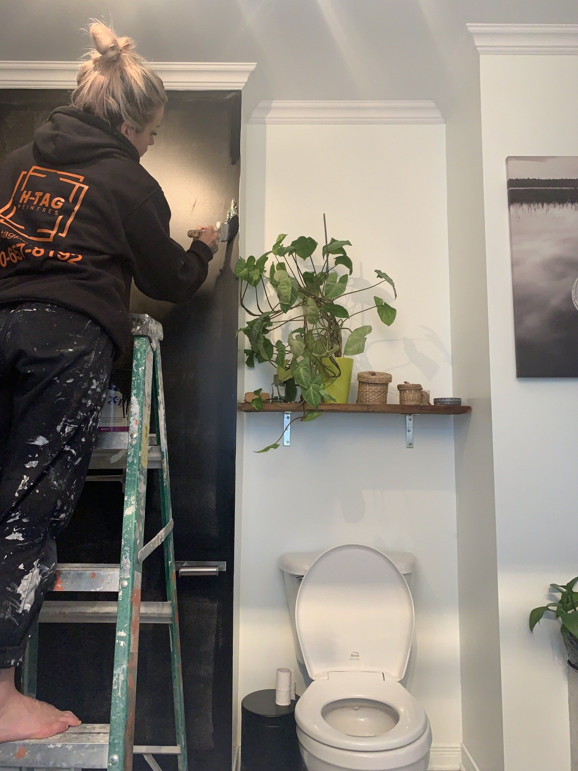 Une femme est debout sur une échelle en train de peindre un mur dans une salle de bain