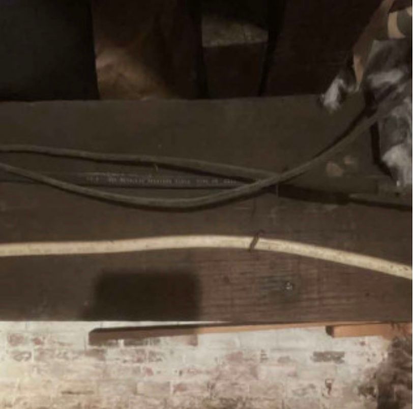 A cat is sitting on a wooden table with a bunch of wires hanging from it.