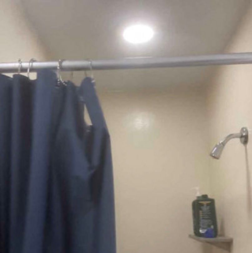 A shower with a blue shower curtain and a shower head.