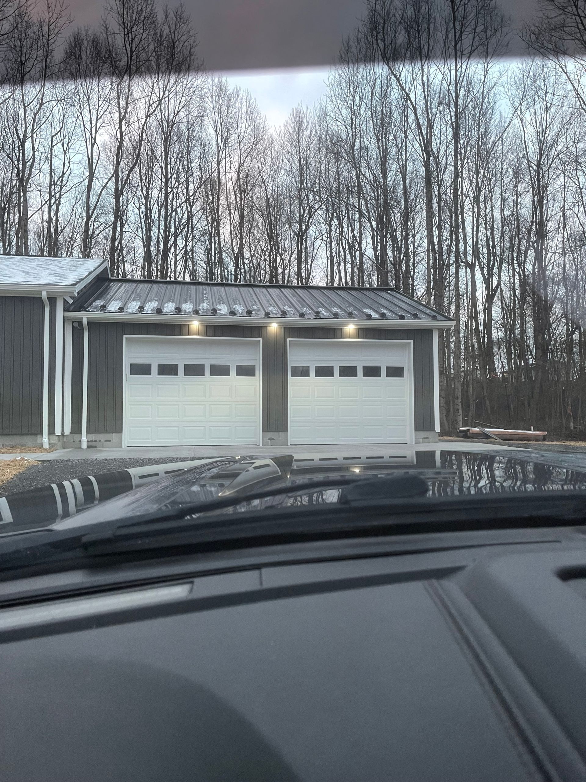 A car is parked in front of a garage with two garage doors.