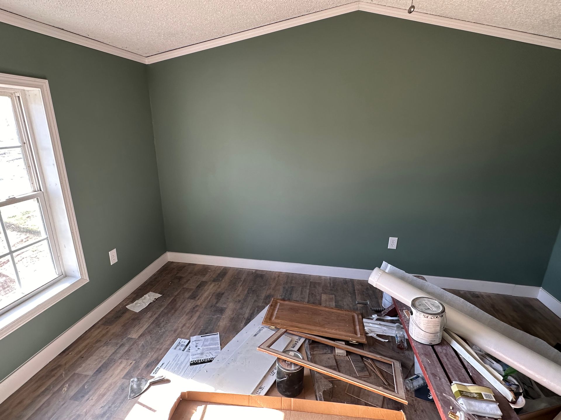 A room with green walls and wooden floors is being painted.