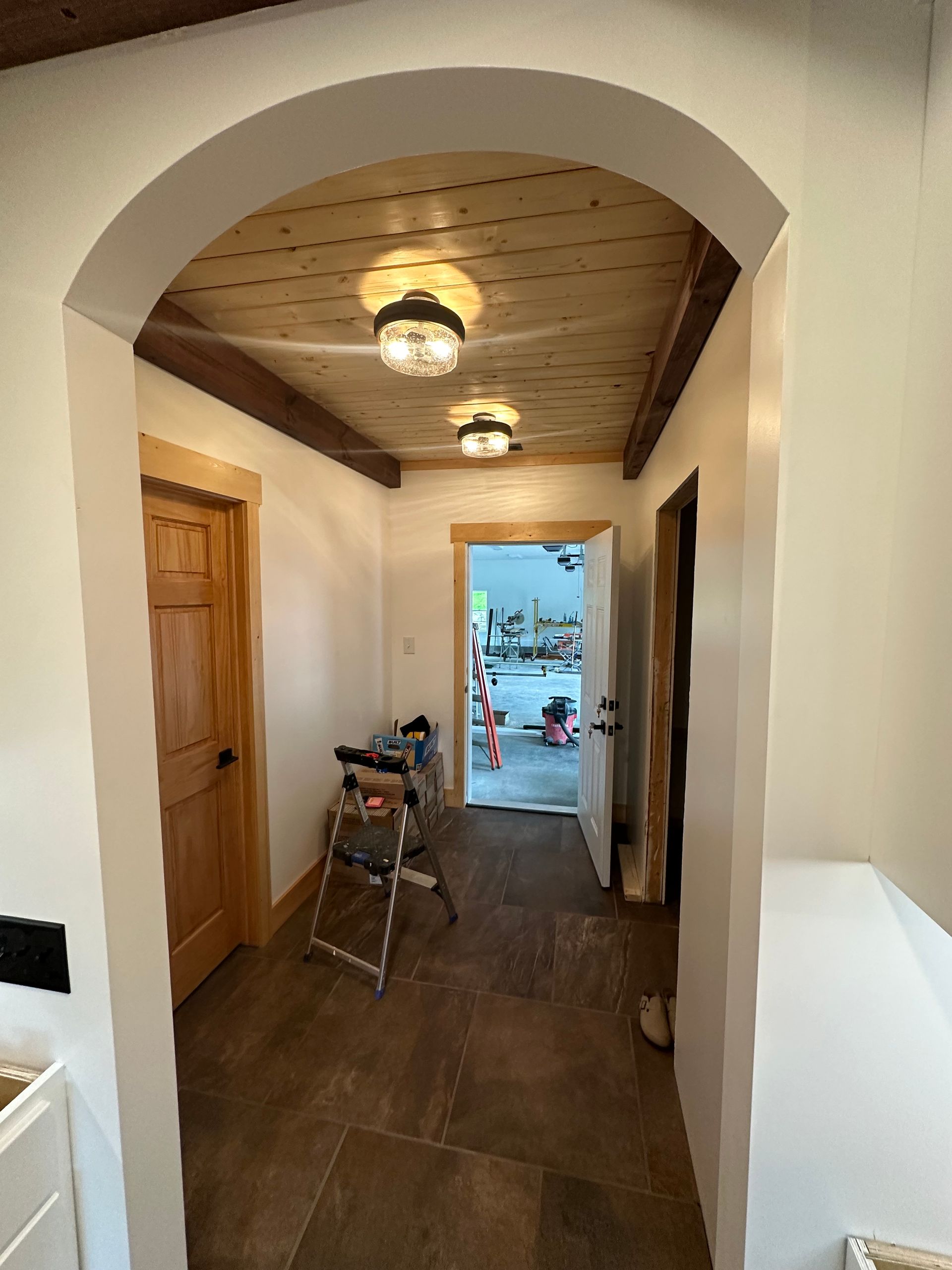 A hallway with a wooden ceiling and arched doorway leading to a kitchen.