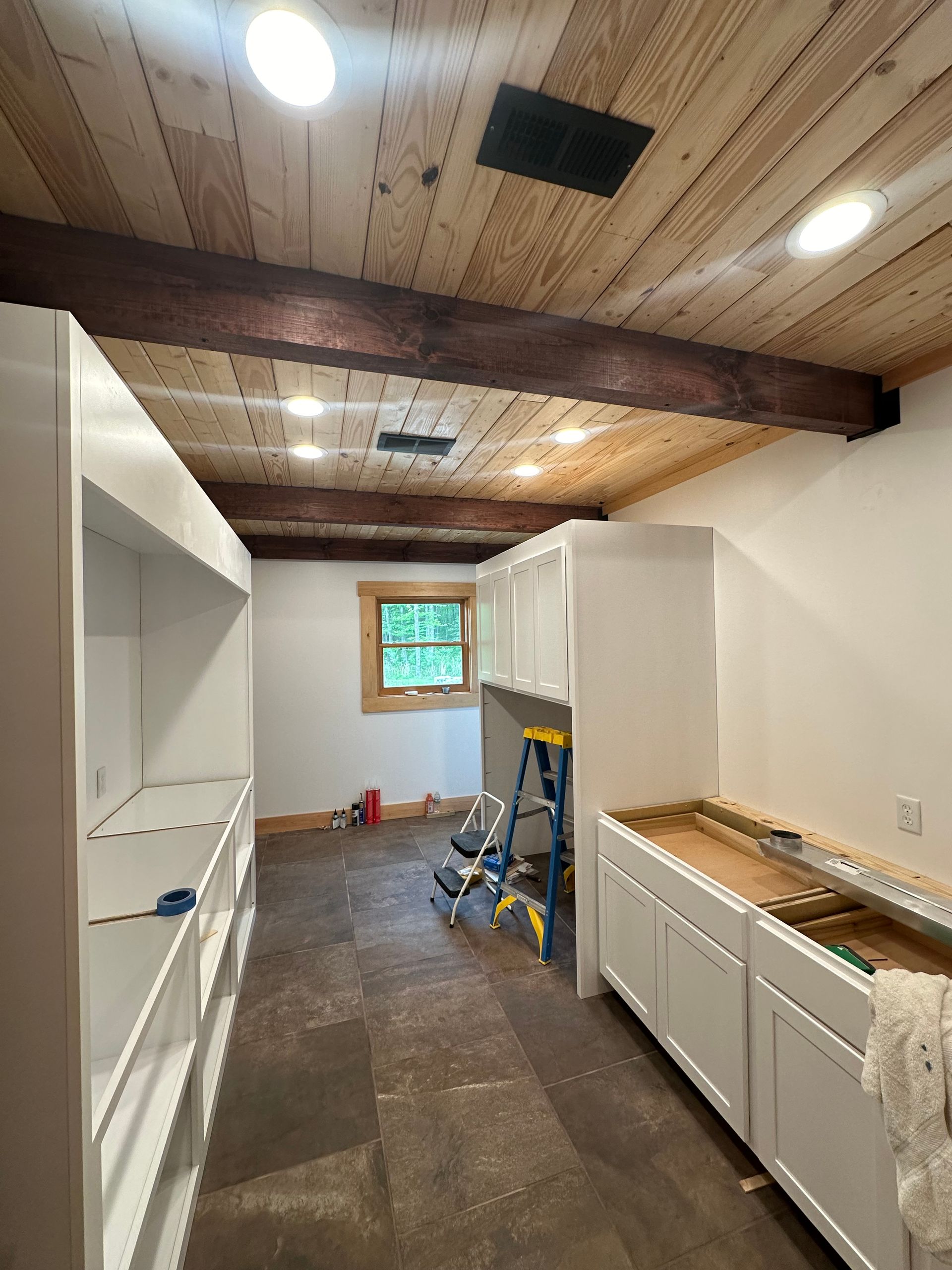 A kitchen under construction with white cabinets and a wooden ceiling.