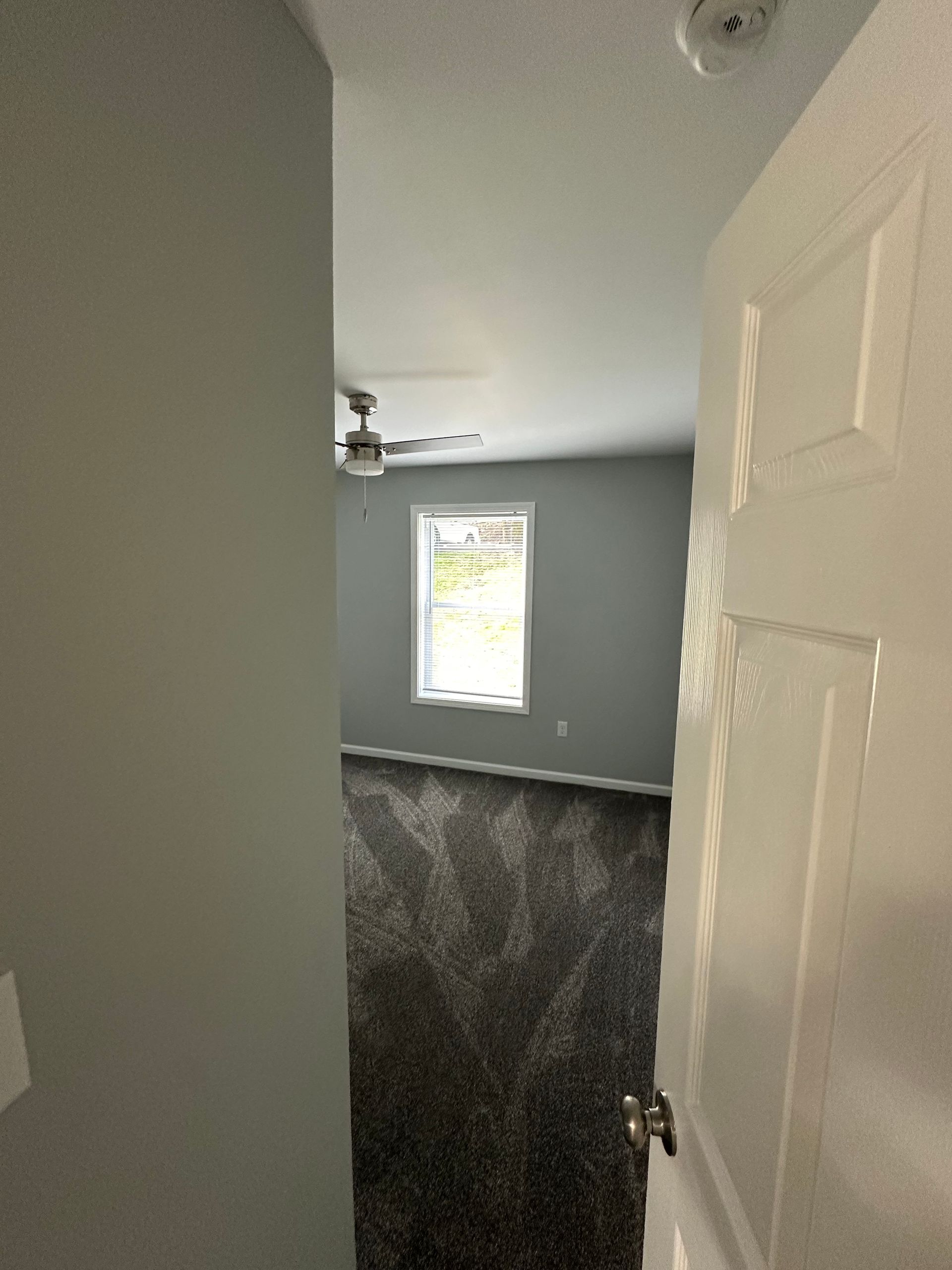 A bedroom with a ceiling fan and a window.