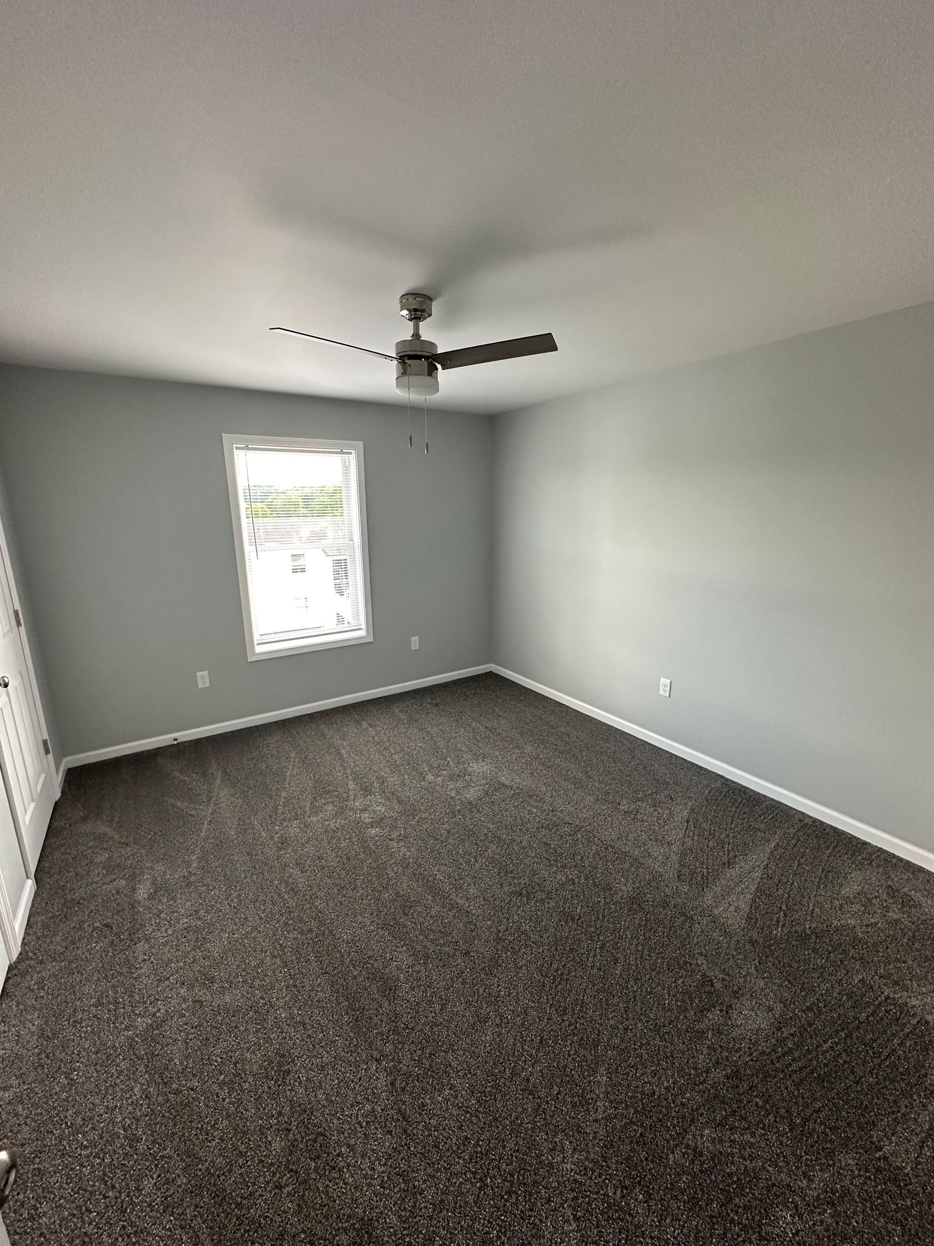 An empty bedroom with a ceiling fan and a window.