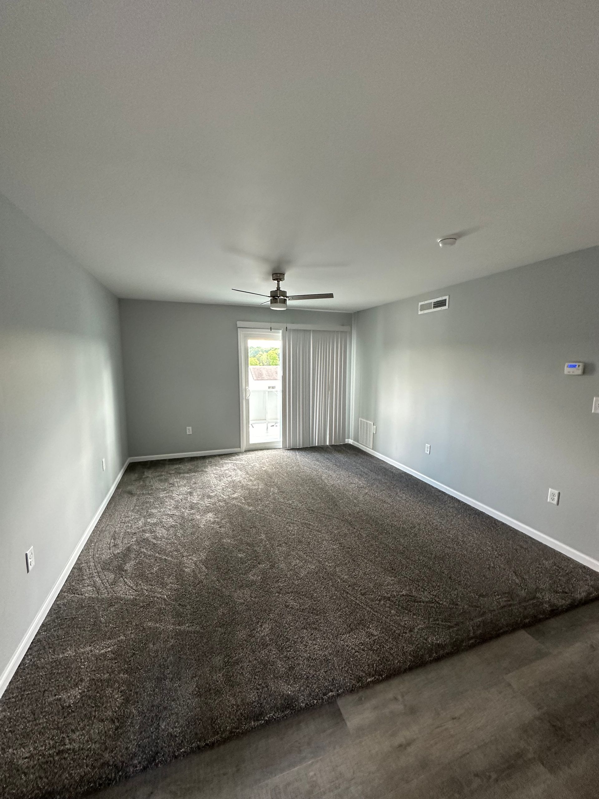 An empty living room with a ceiling fan and a sliding glass door.