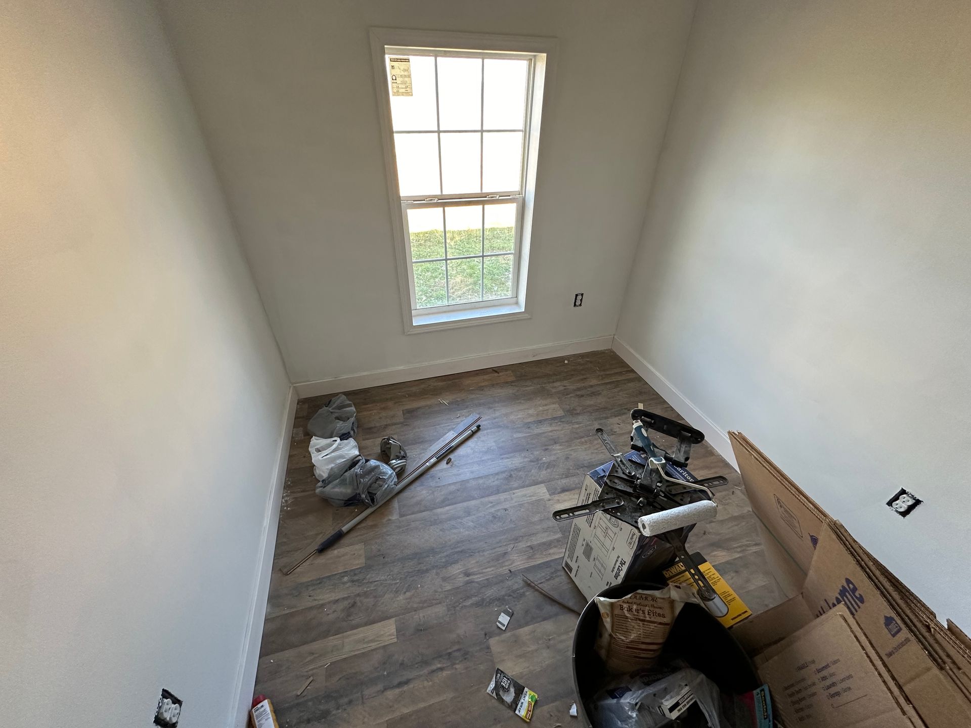 A room with a window and wooden floors is being remodeled.