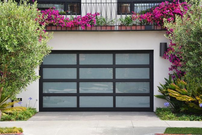 A white house with a black garage door and purple flowers on the balcony.