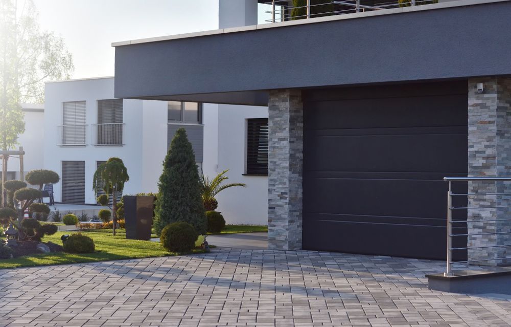 A modern house with a black garage door and a brick driveway.