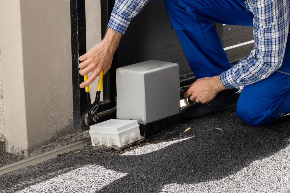 A man is kneeling down to fix a sliding gate.