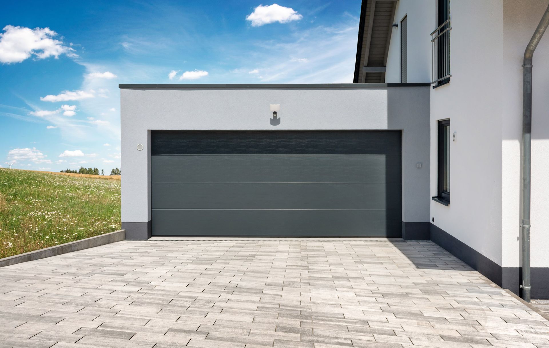 A gray garage door is sitting in front of a white house.