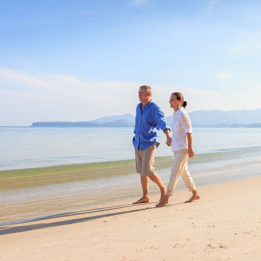A man and a woman are walking barefoot on the beach