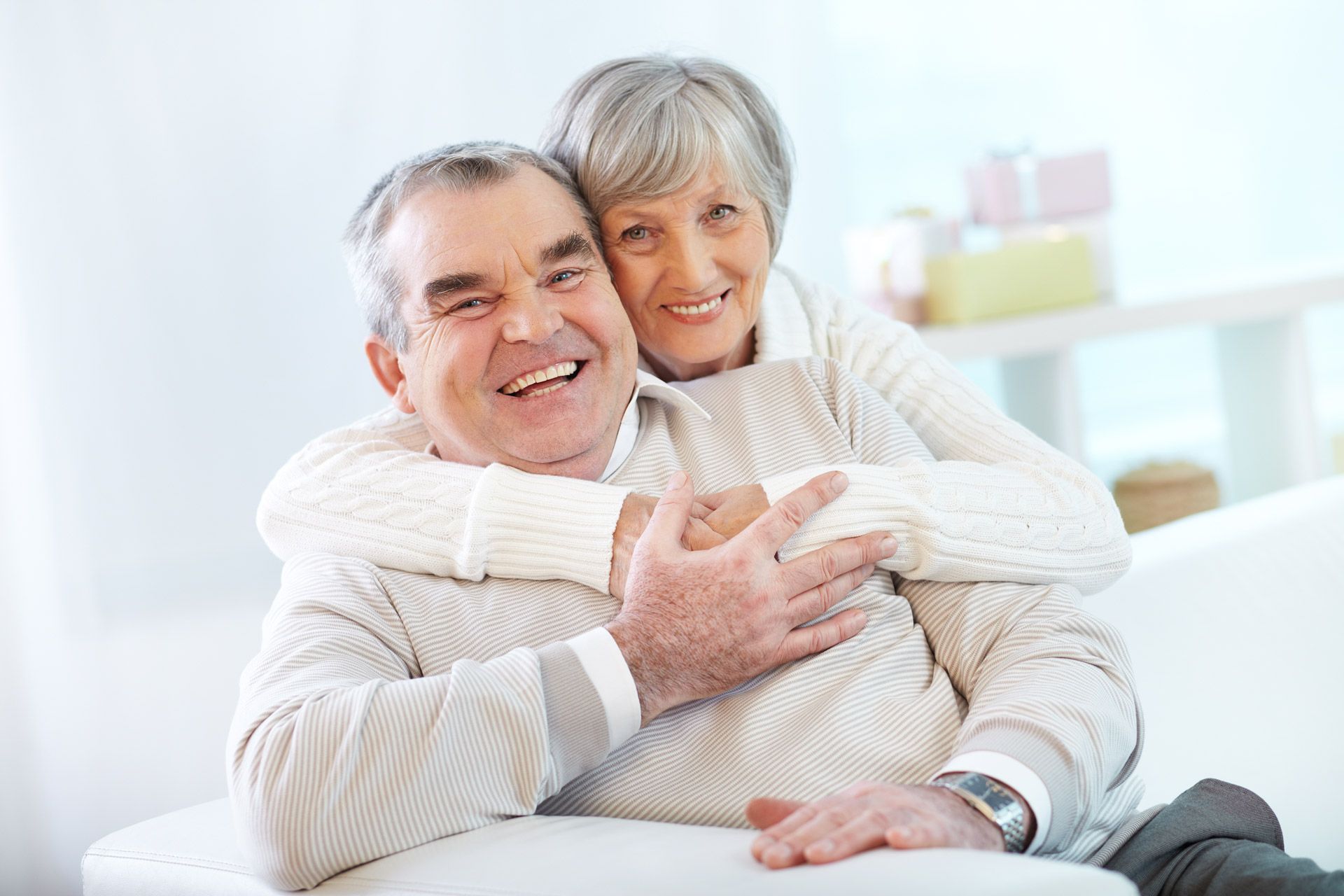 An elderly couple is sitting on a couch and hugging each other.