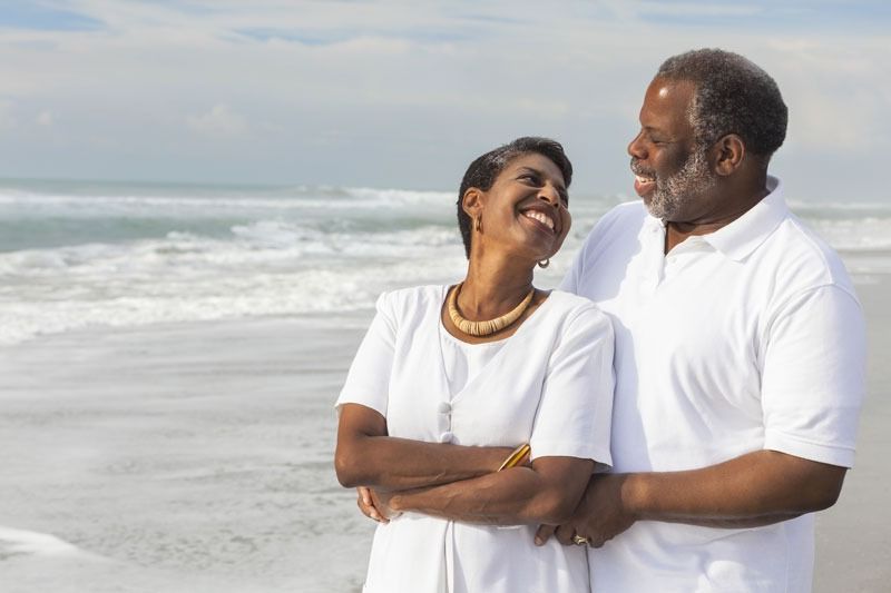A man and a woman are standing on the beach looking at the ocean.