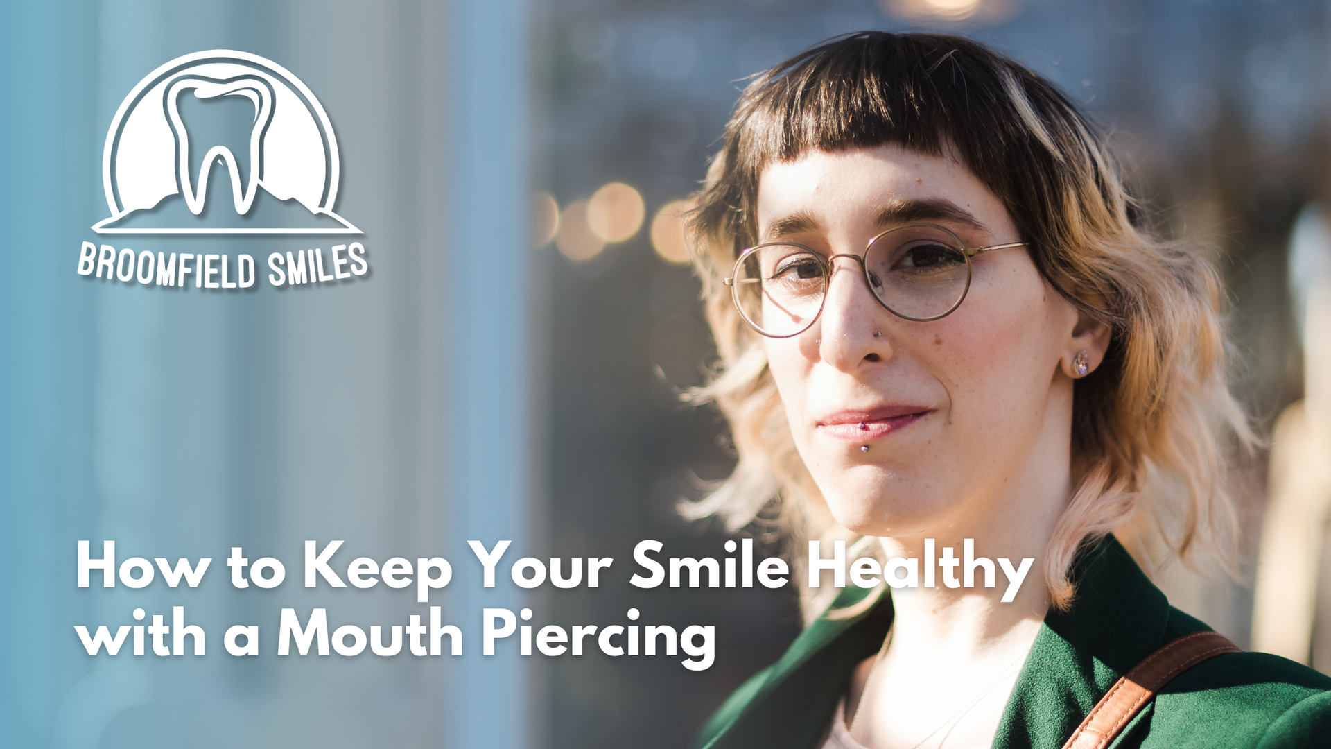 A woman with glasses and a mouth piercing is smiling.