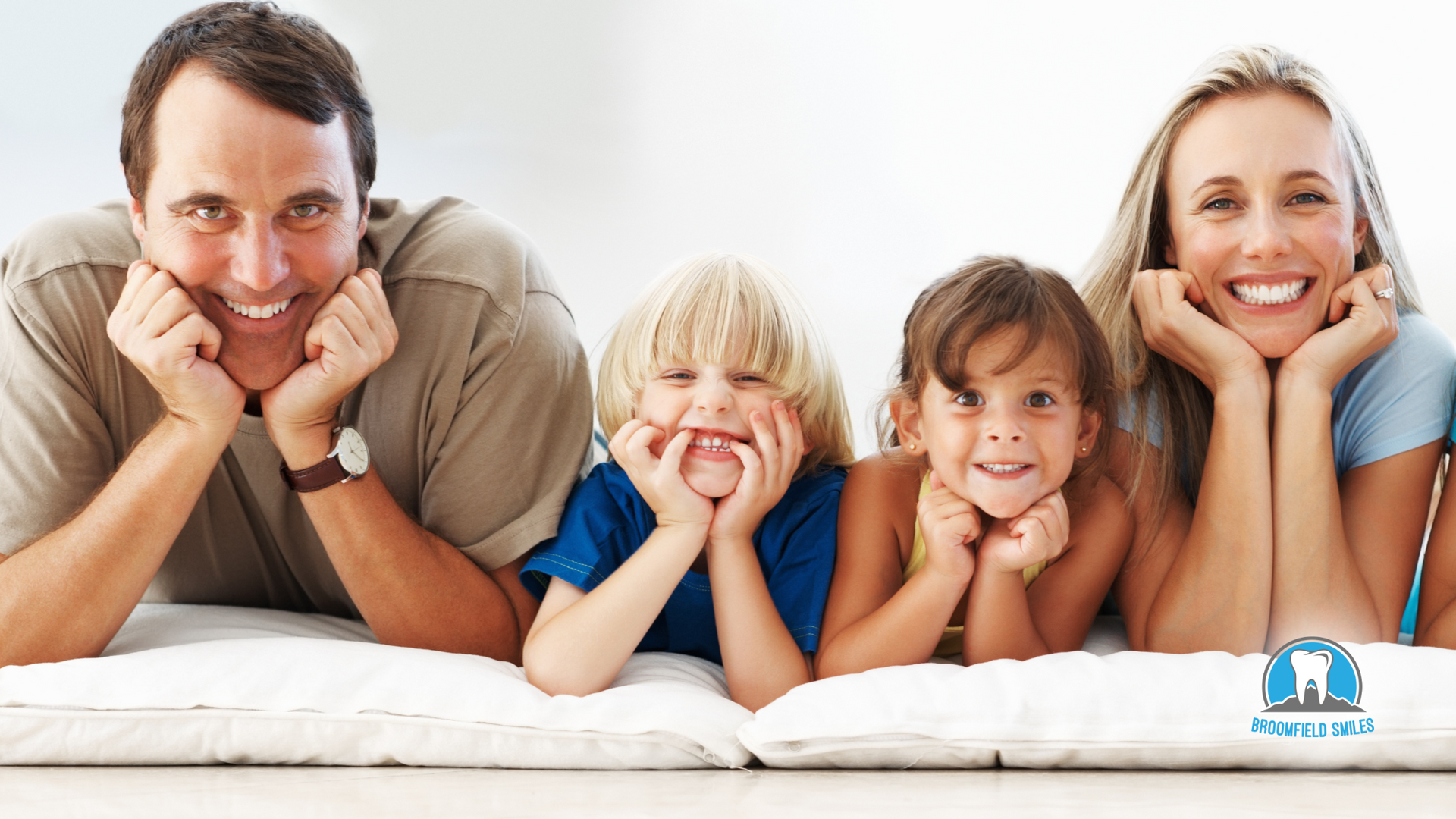 A family is laying on a bed with their hands on their faces.
