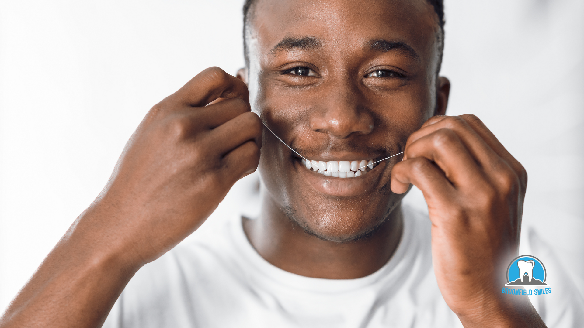 A man is flossing his teeth and smiling.