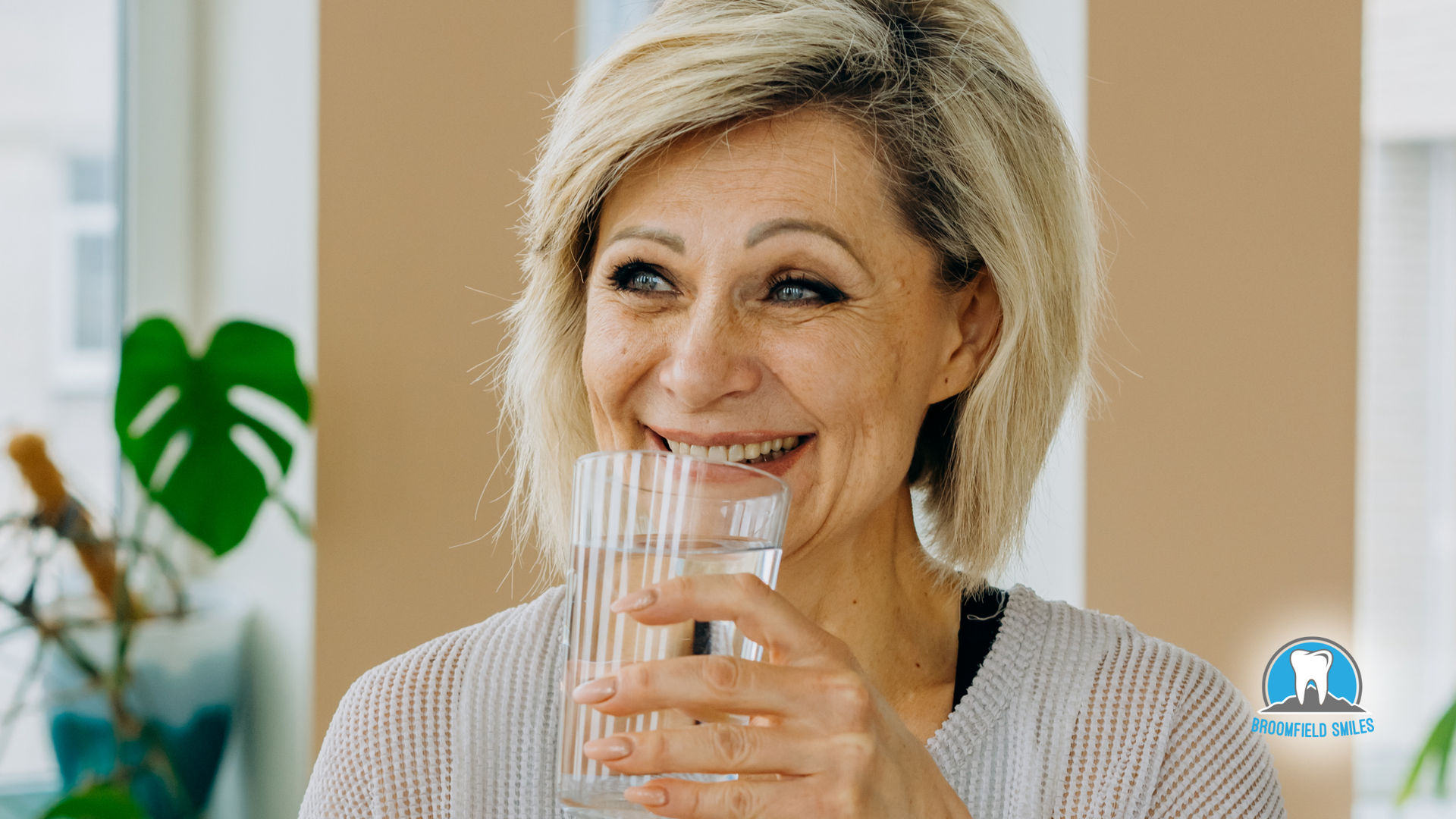 A woman is drinking a glass of water and smiling.