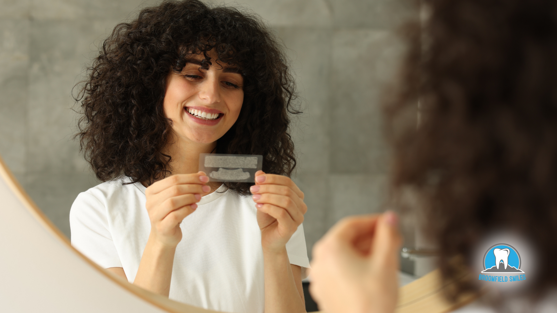A woman is smiling while looking at her teeth in the mirror.