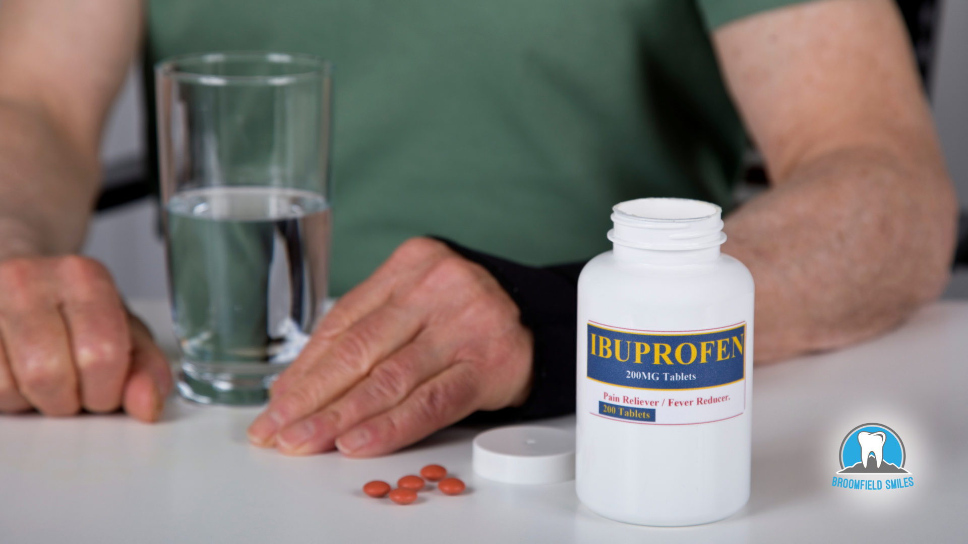 A man is sitting at a table with a bottle of ibuprofen and a glass of water.