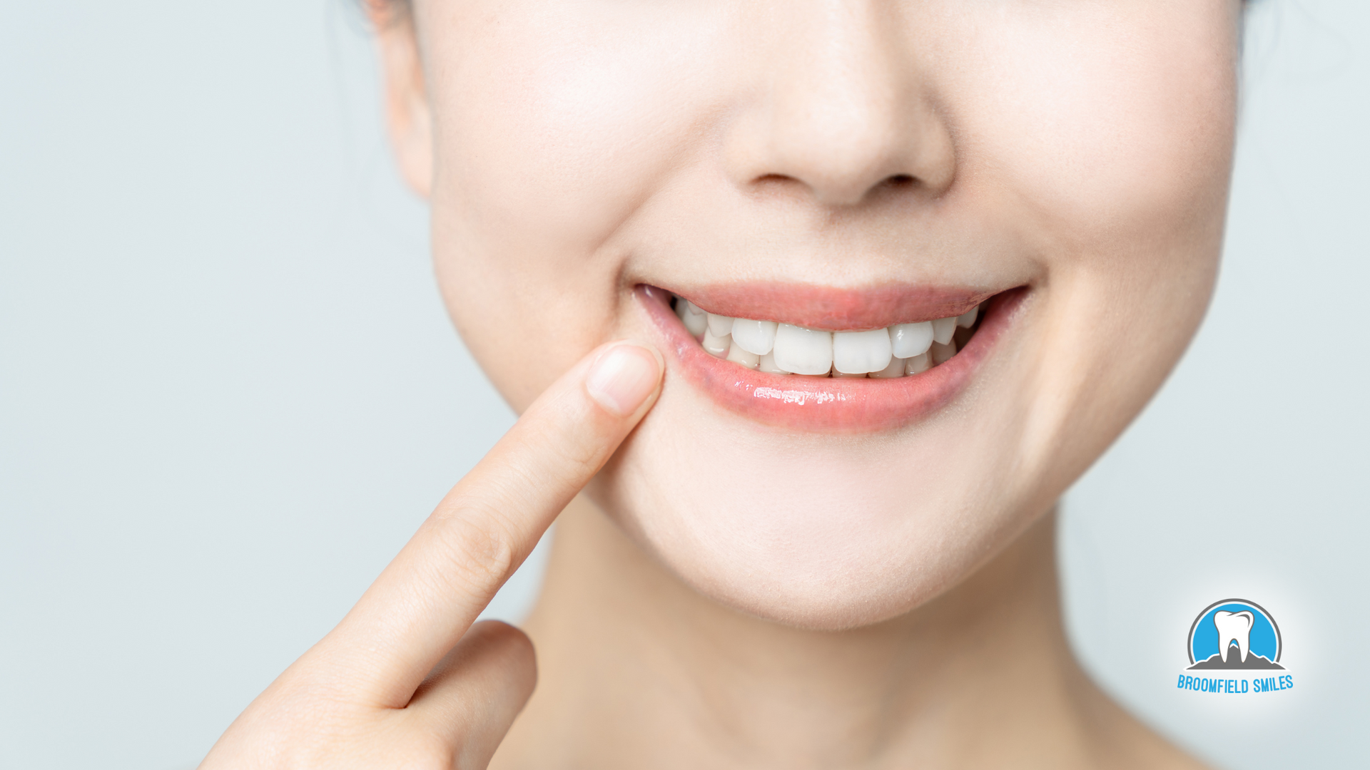 A woman is smiling and pointing at her teeth with her finger.
