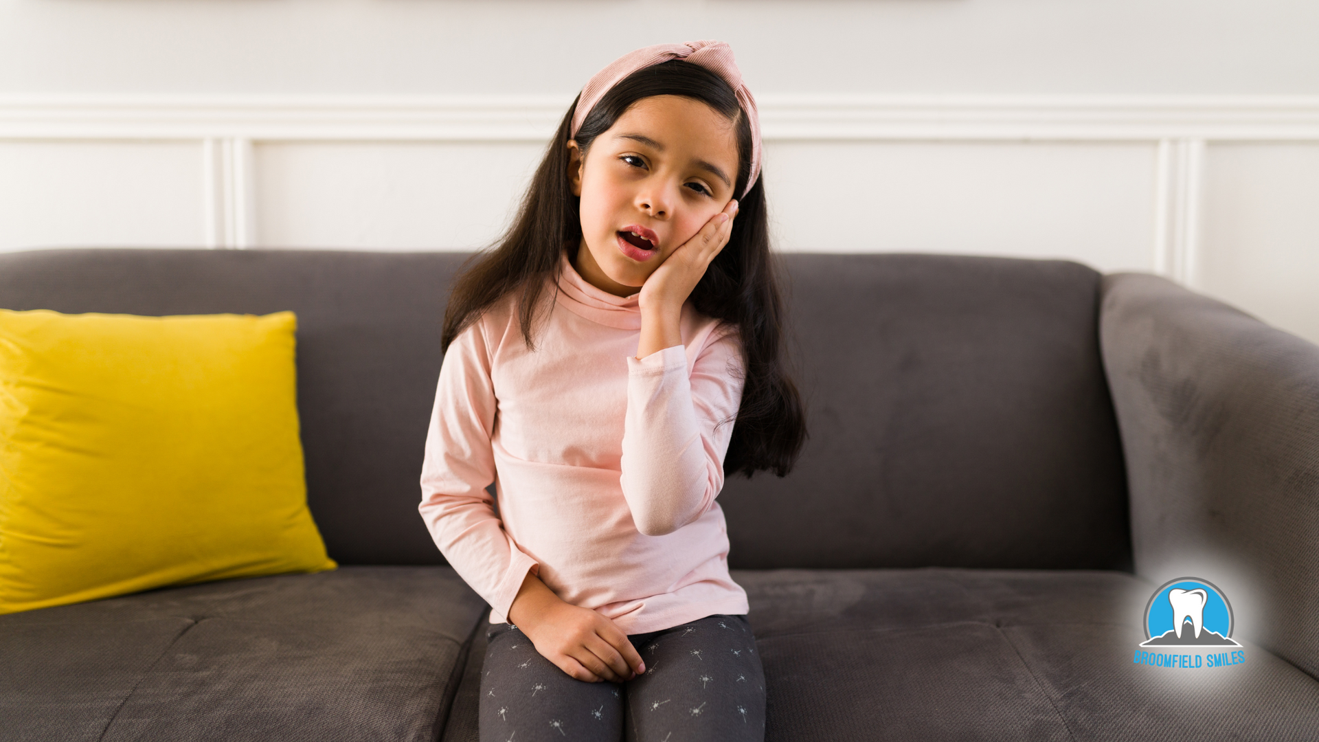 A little girl is sitting on a couch with a toothache.