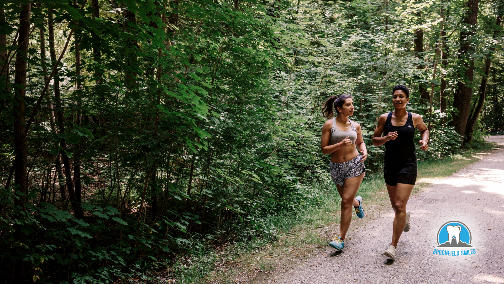 Two women are running on a dirt path in the woods.