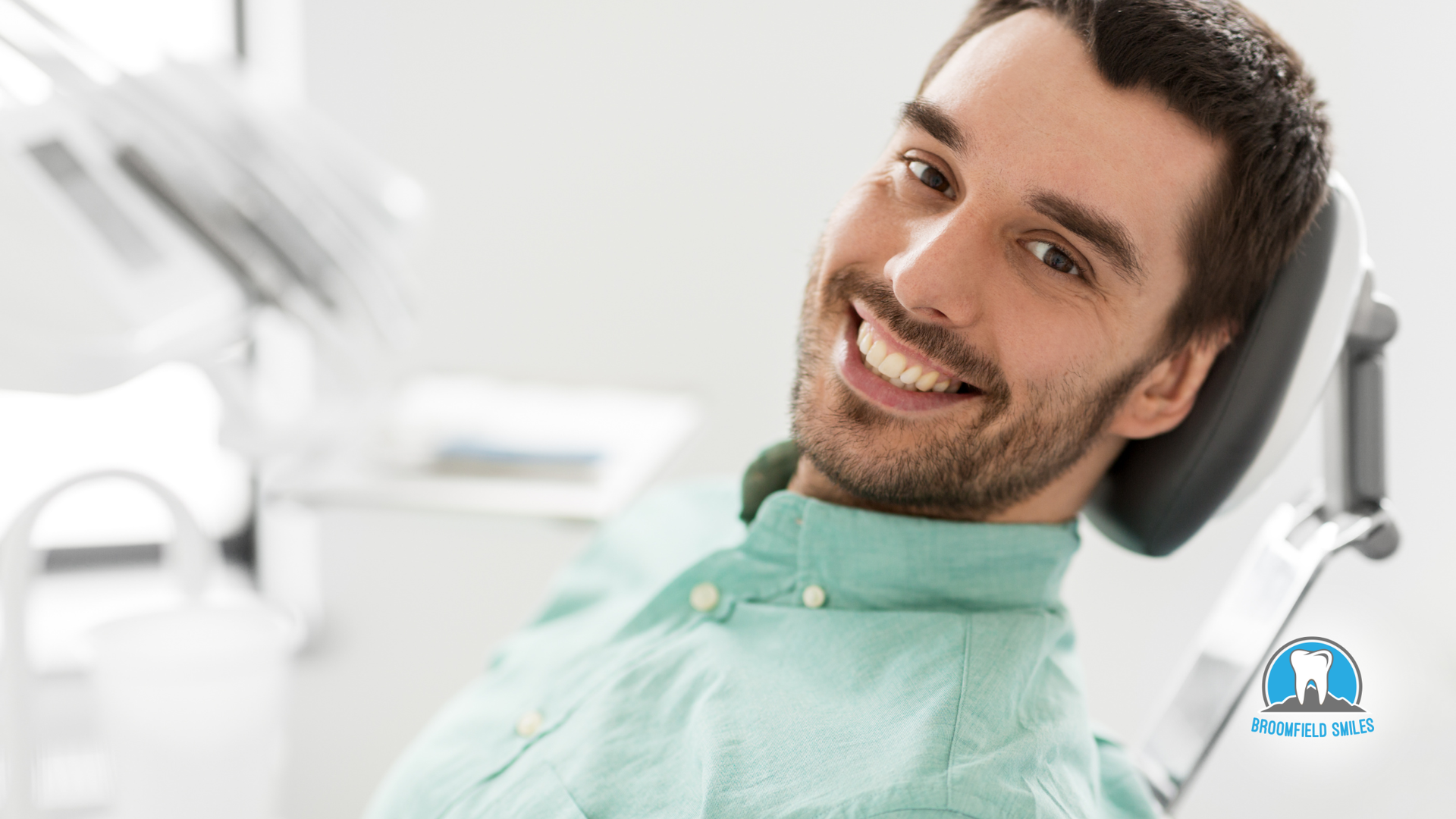 Man smiling in a dentist's chair with dental tools in the background.