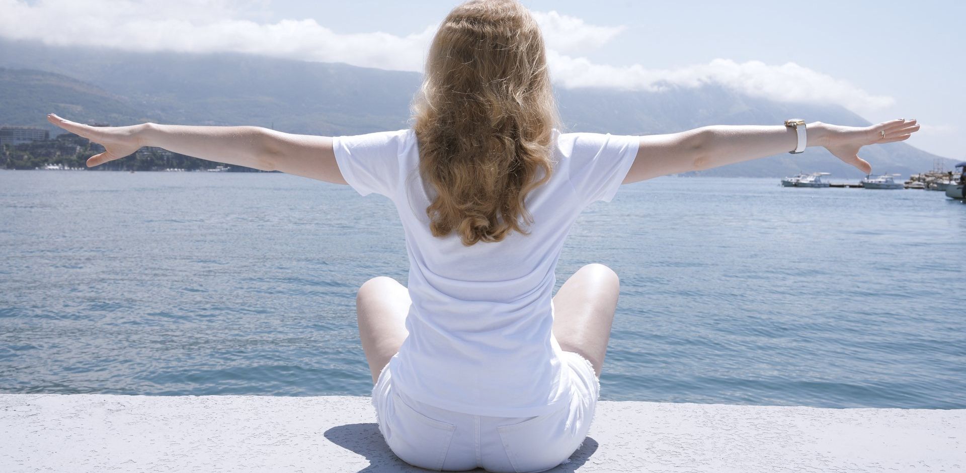 Woman is sitting on a pier with her arms outstretched. Regenerative therapy and PRP therapy are providing a new option for addressing back pain.