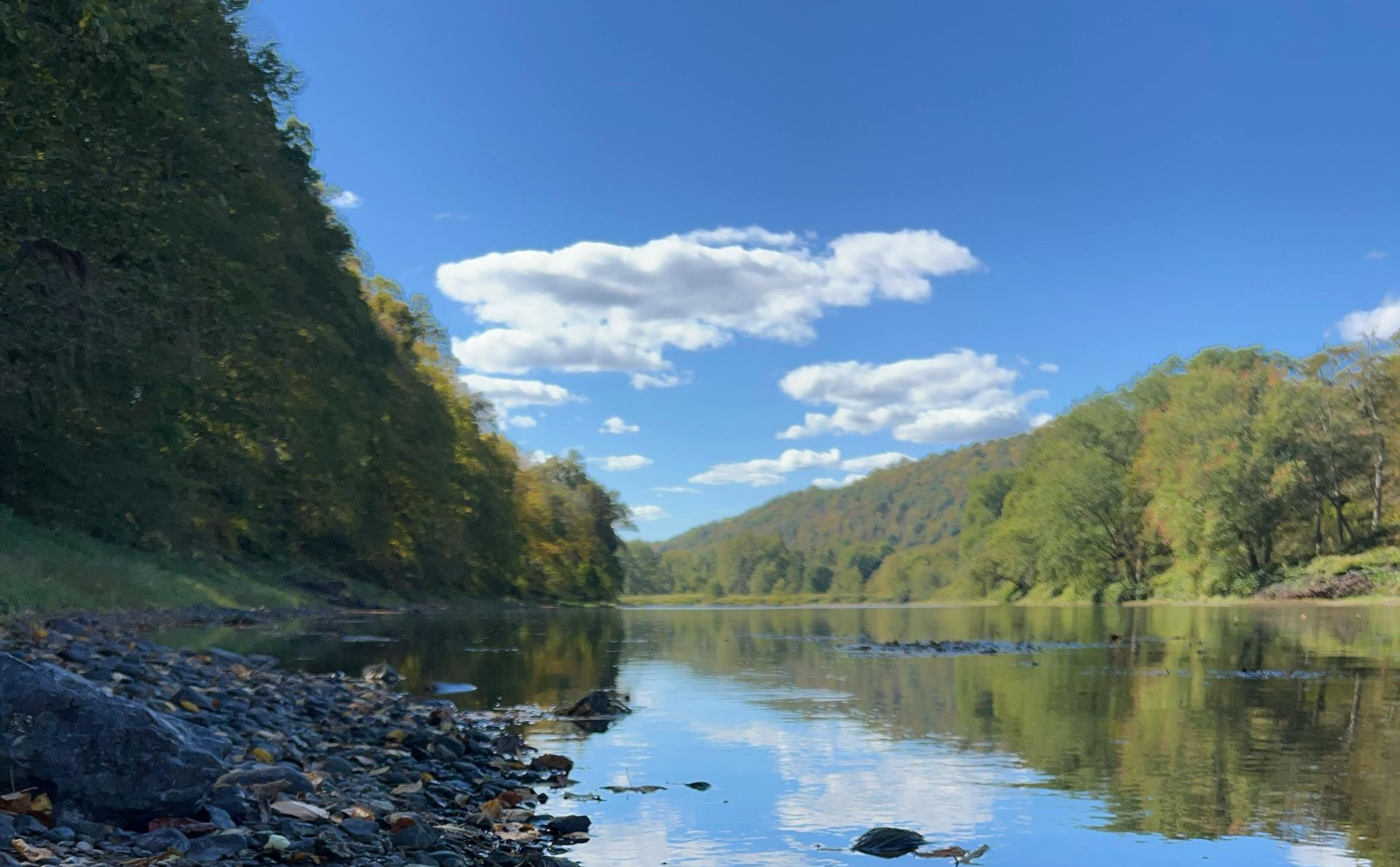 Rocky shoreline with a calm river reflecting a blue sky and trees.