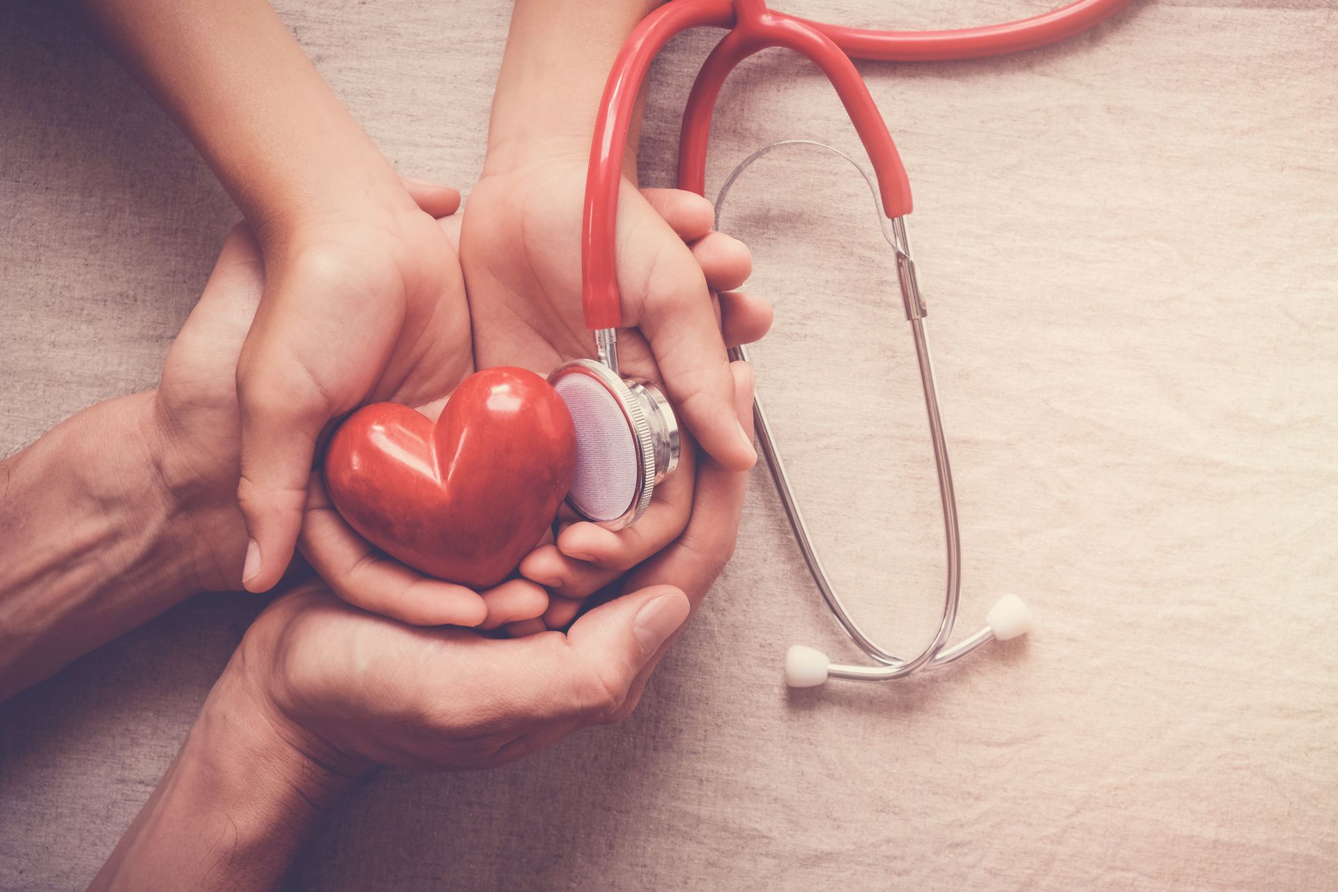 Hands holding a red heart and stethoscope, suggesting health care.