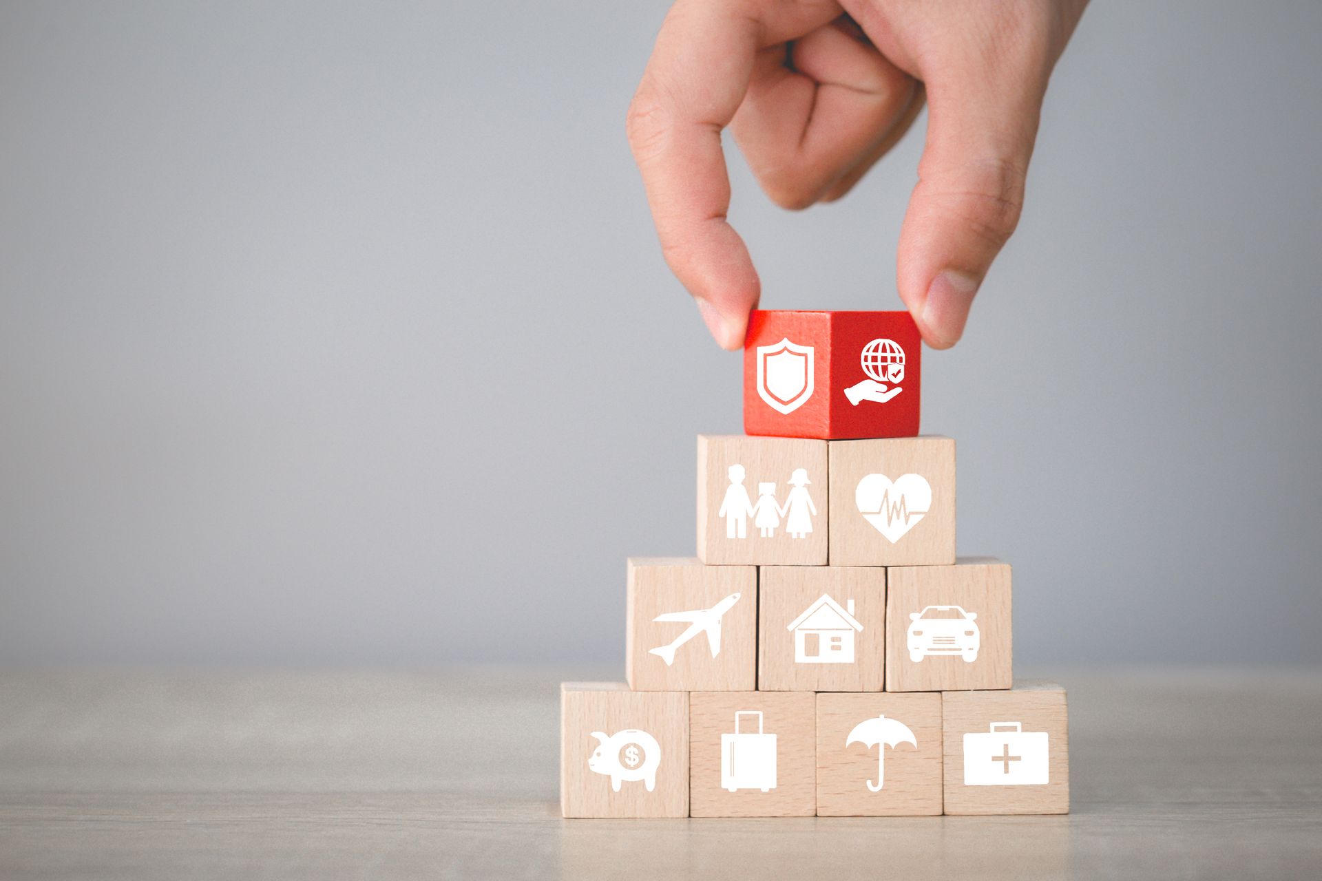 Hand placing insurance-themed block on a pyramid of blocks with various icons.