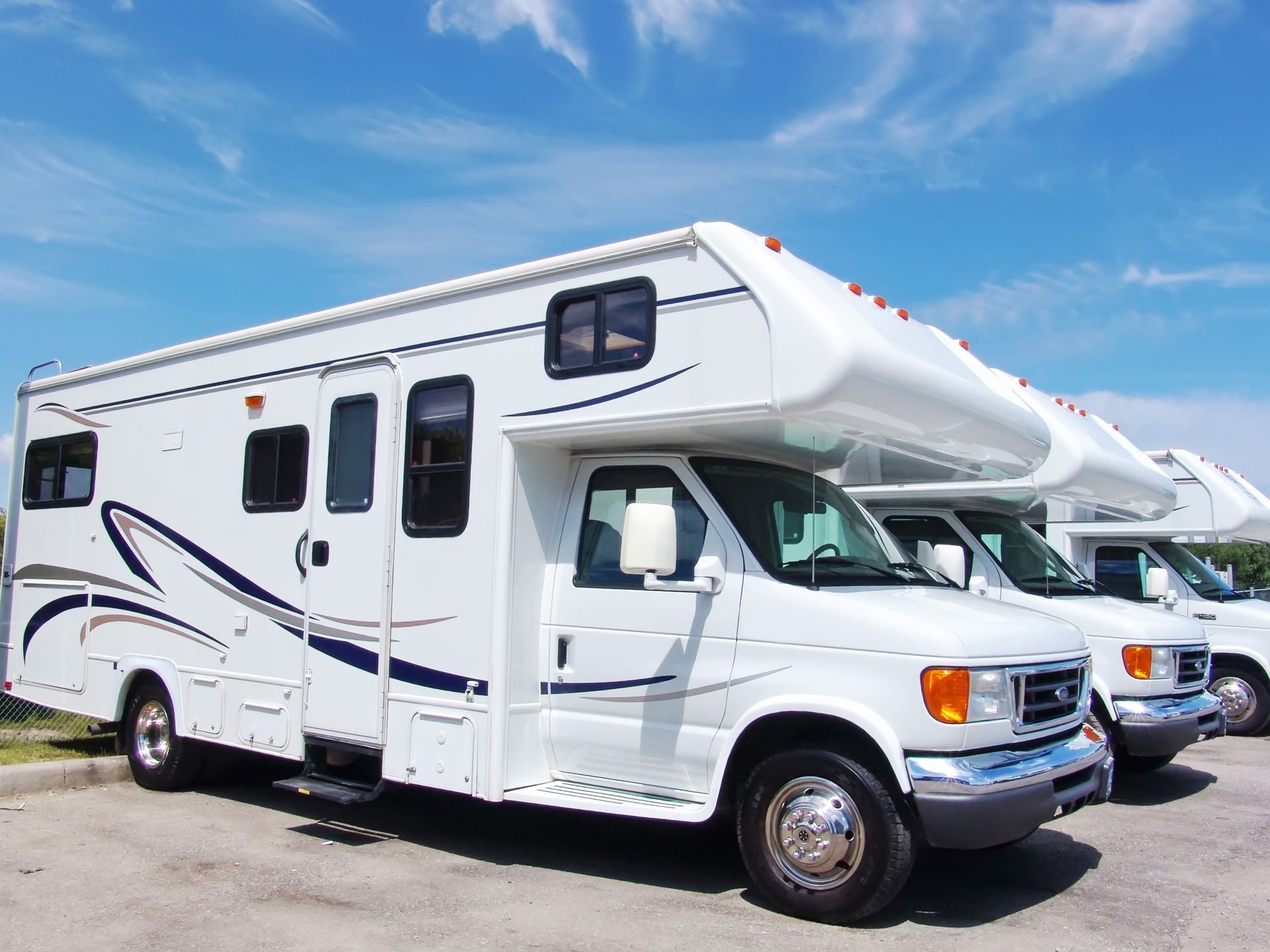 White RVs parked in a row against a blue sky.
