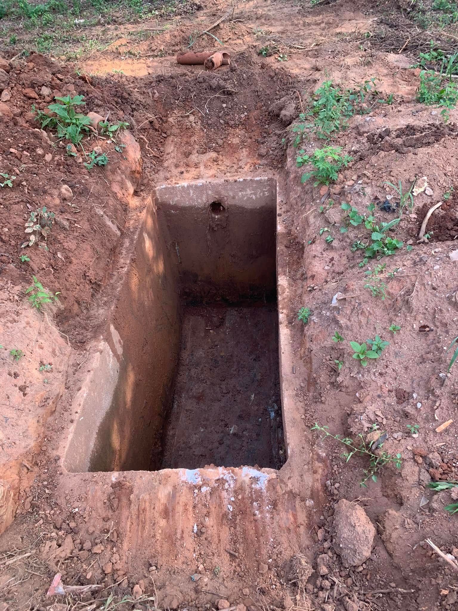 Open rectangular concrete structure in a dirt hole. Green grass surrounds the hole.