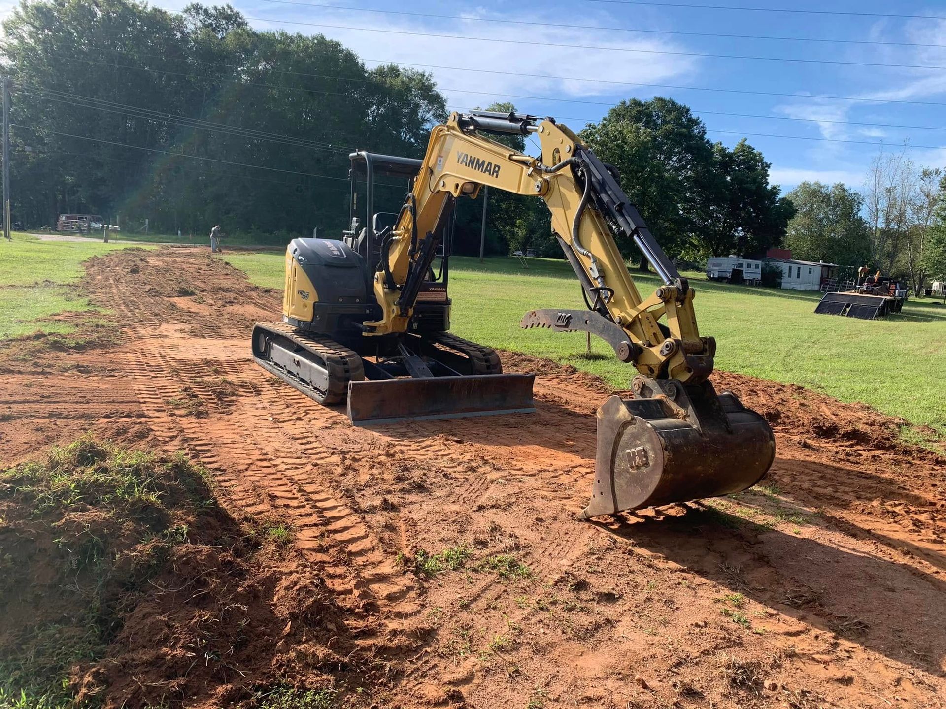 Yellow and black excavator on a dirt path in a grassy area, digging soil.