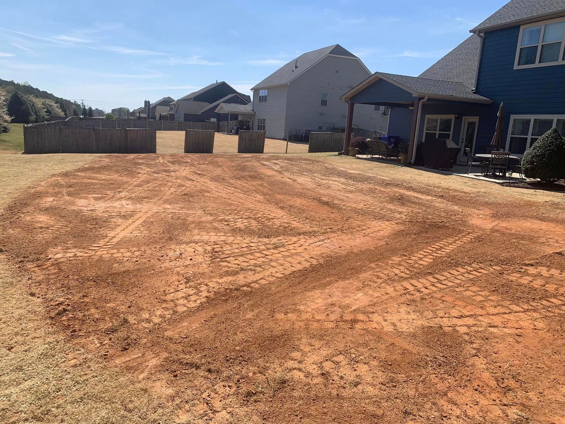 Cleared backyard dirt area with tire tracks, houses in background, sunny day.