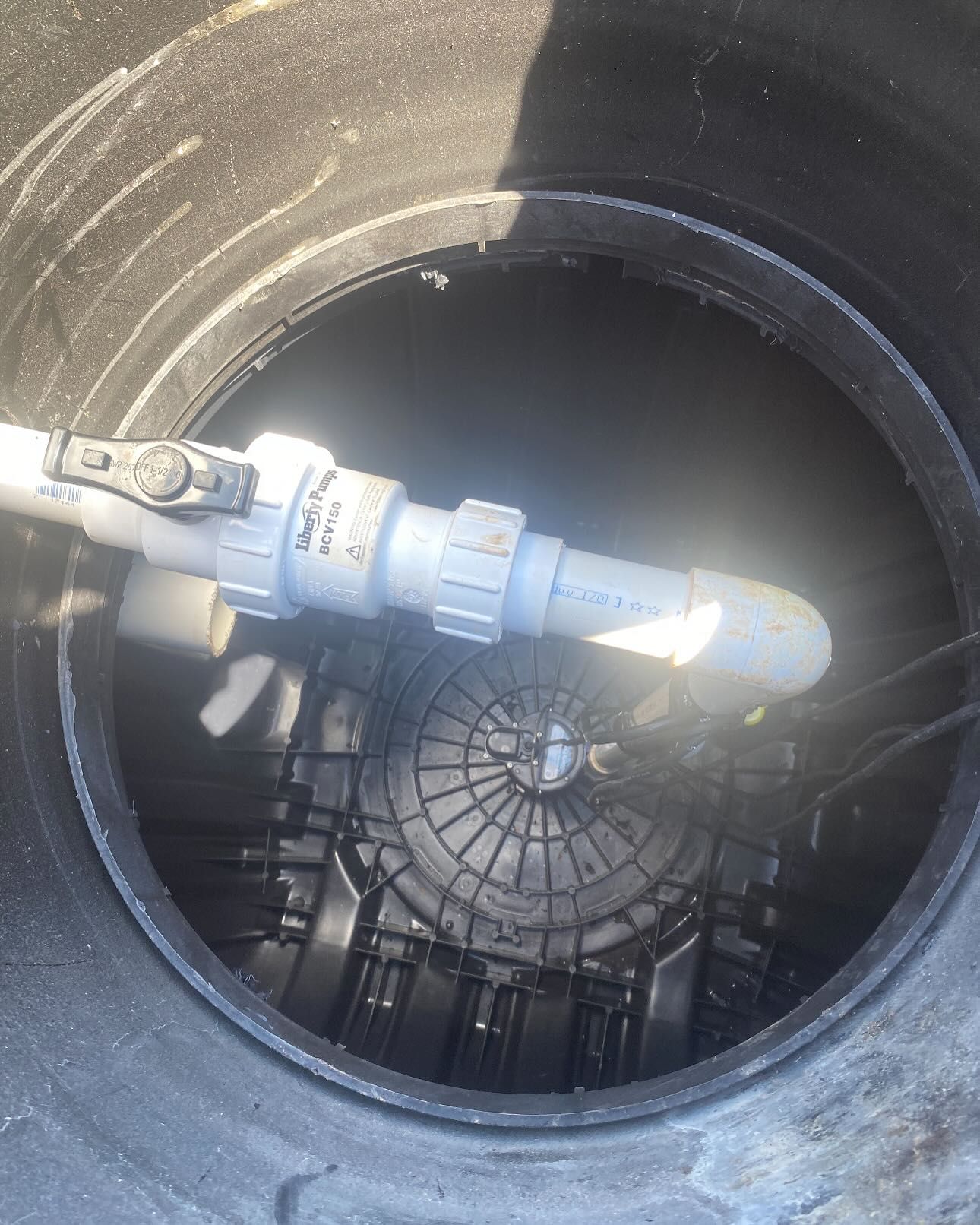 Inside a dark well: PVC pipes, valve, and a black, domed structure.