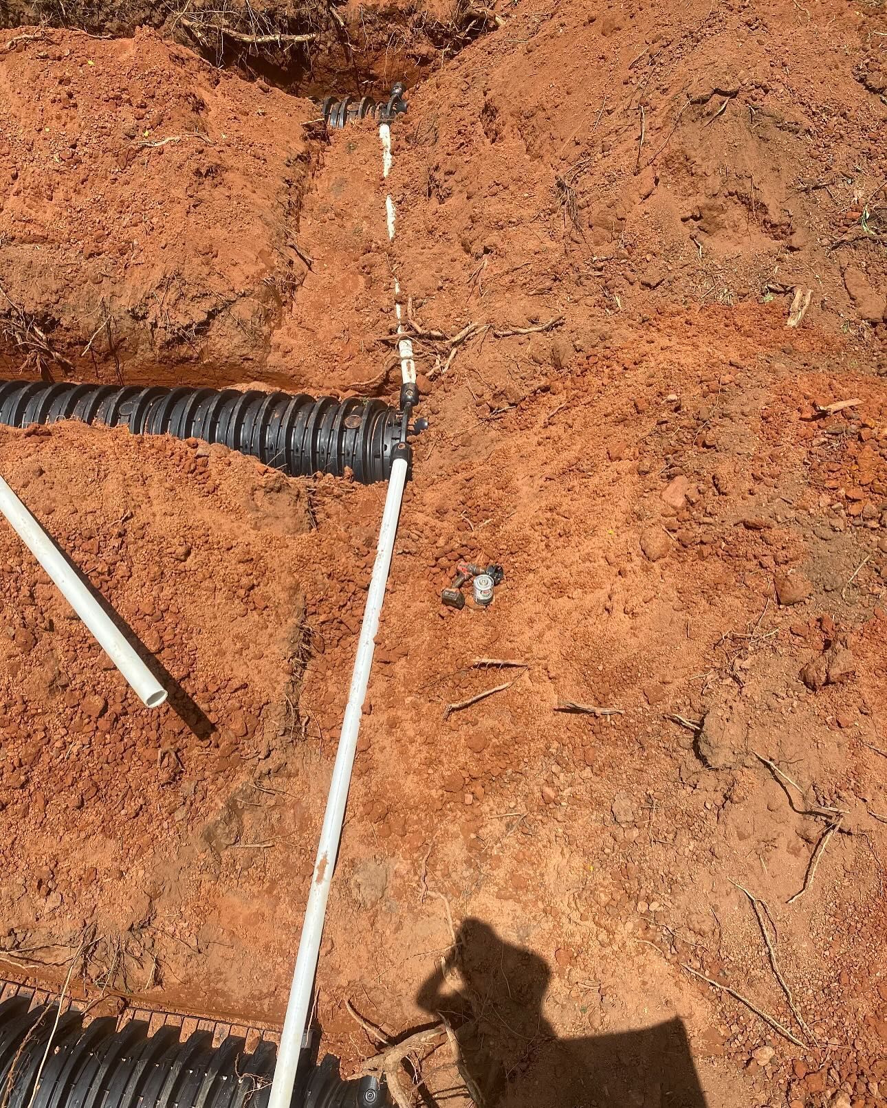 Black corrugated and white PVC pipes in red dirt.