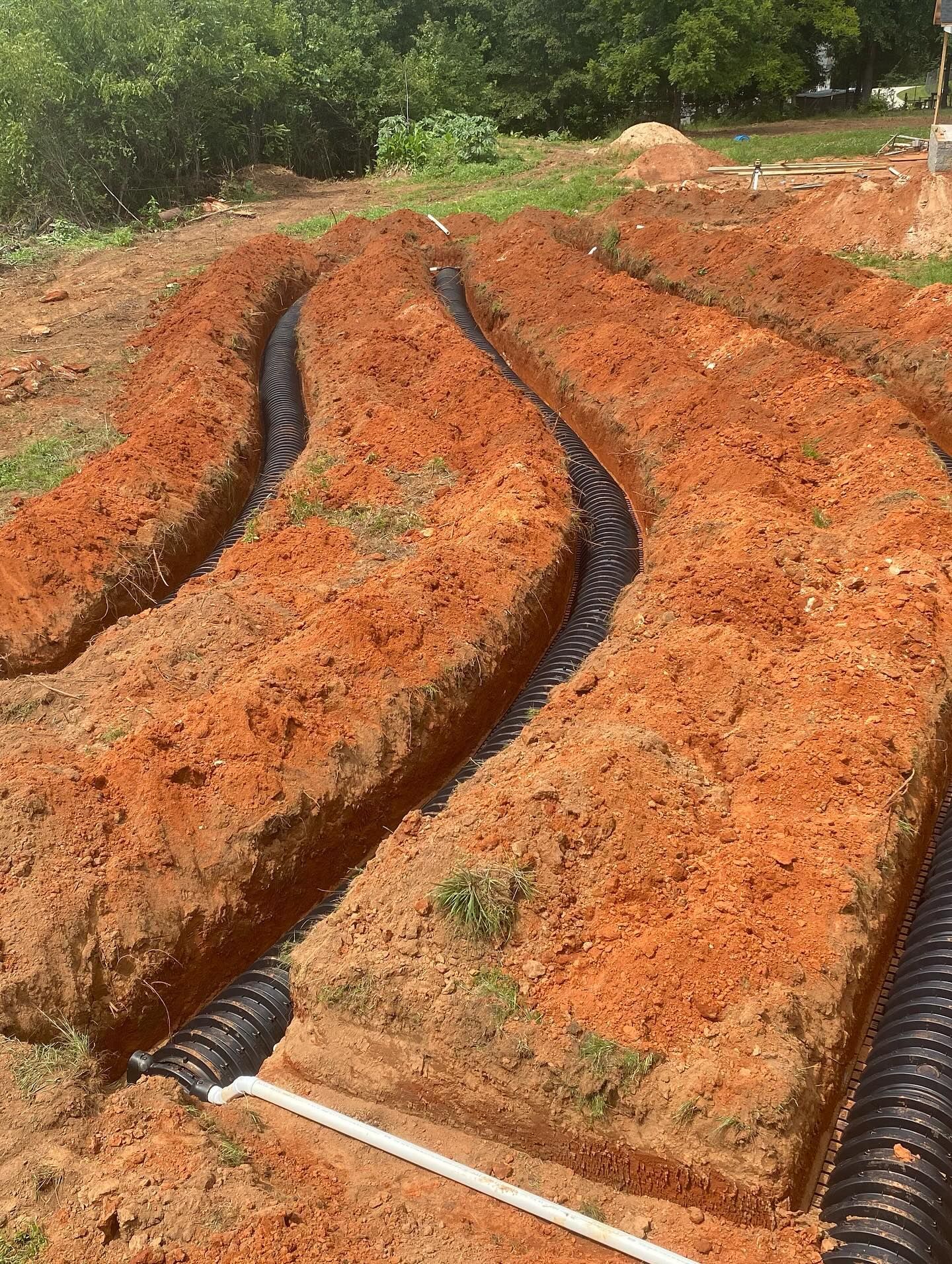 Trenches dug in reddish soil with black pipes laid inside, ready for landscaping.