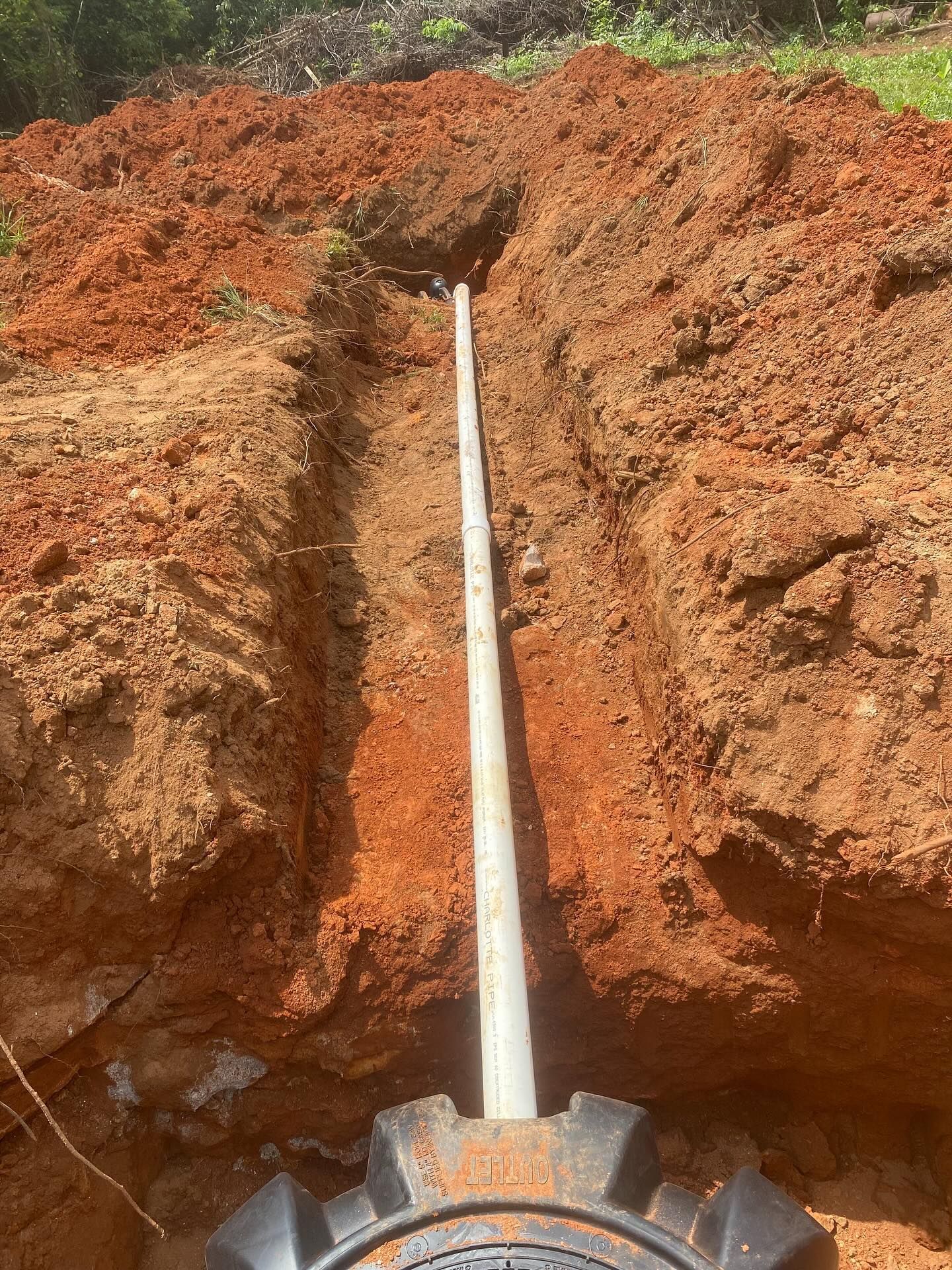 Trench in reddish-brown soil with a white pipe running through it, leading from a black, round object.