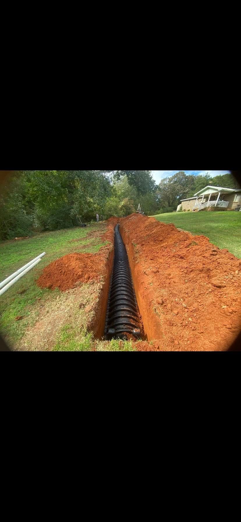 A trench in a yard with black pipe installed, ready for backfill.
