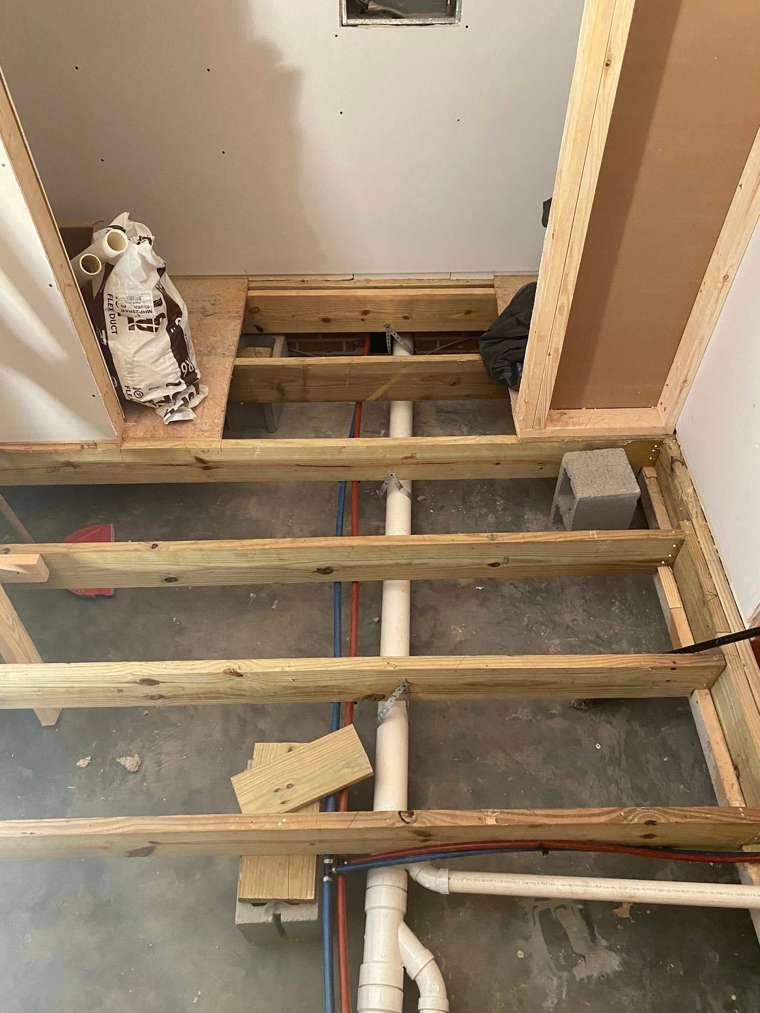 Wooden floor joists and plumbing pipes in a room under construction.