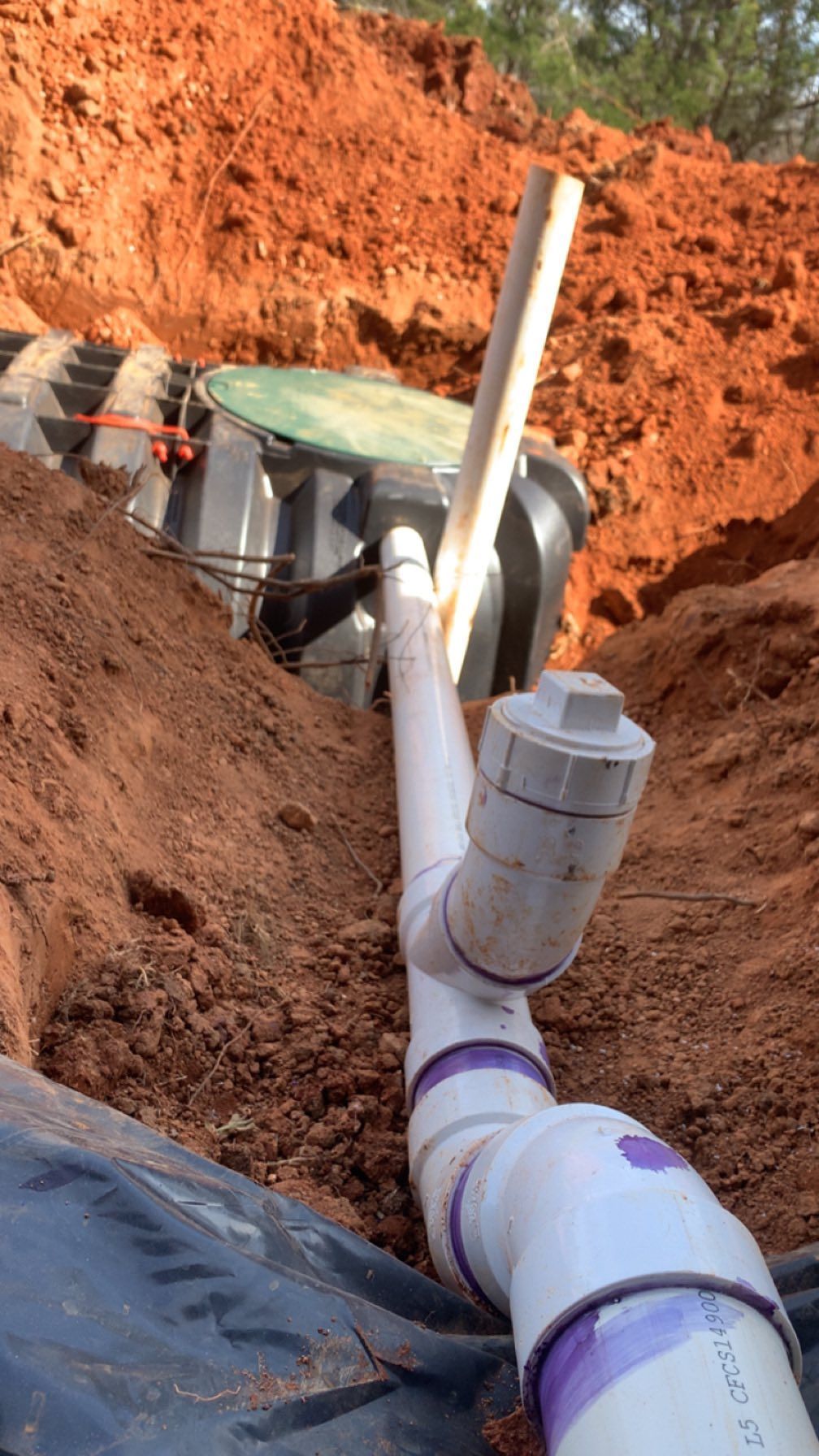 PVC pipes connected to a septic tank buried in red dirt.