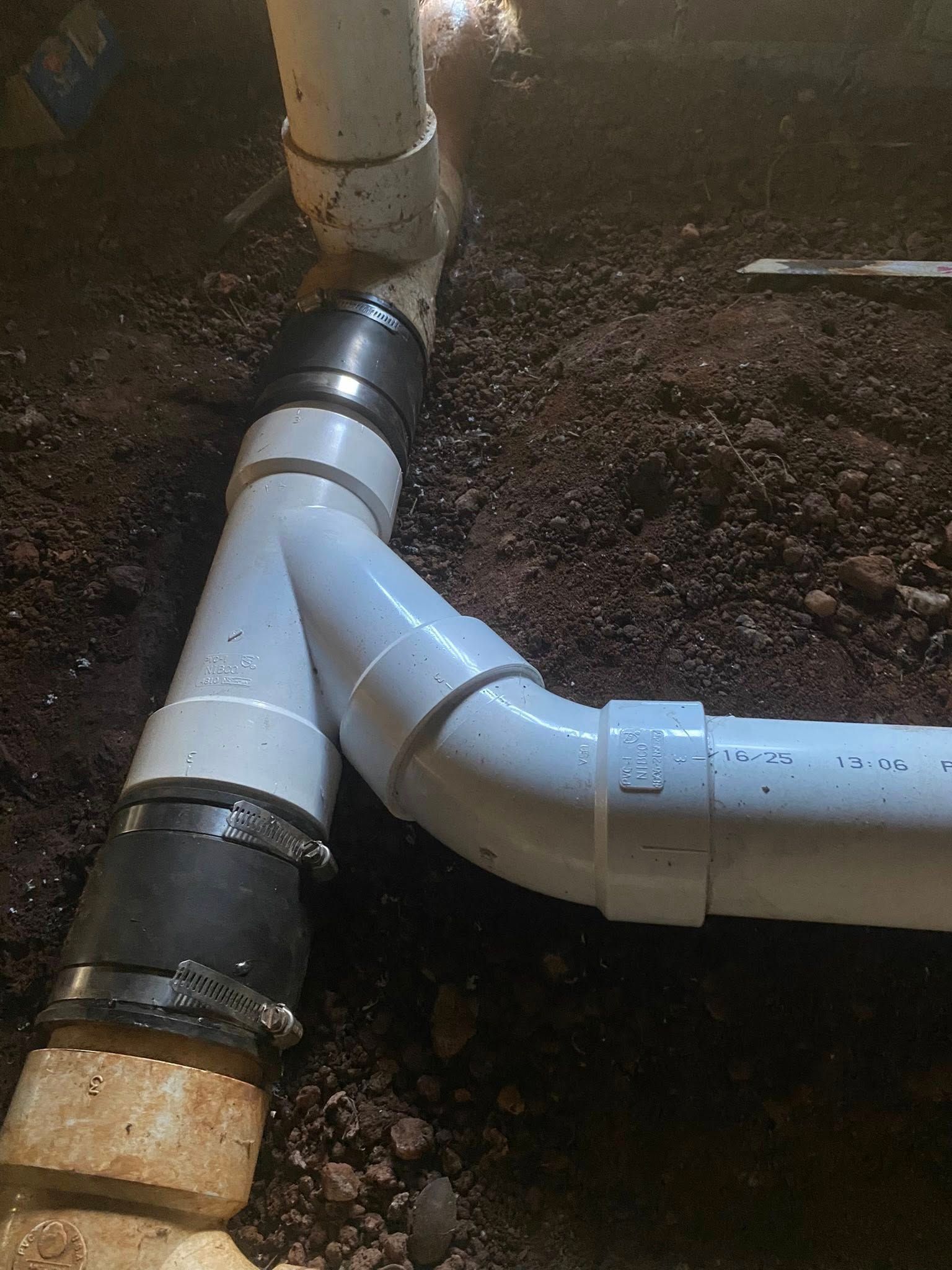 White PVC pipes and fittings connected underground, forming a drainage system.