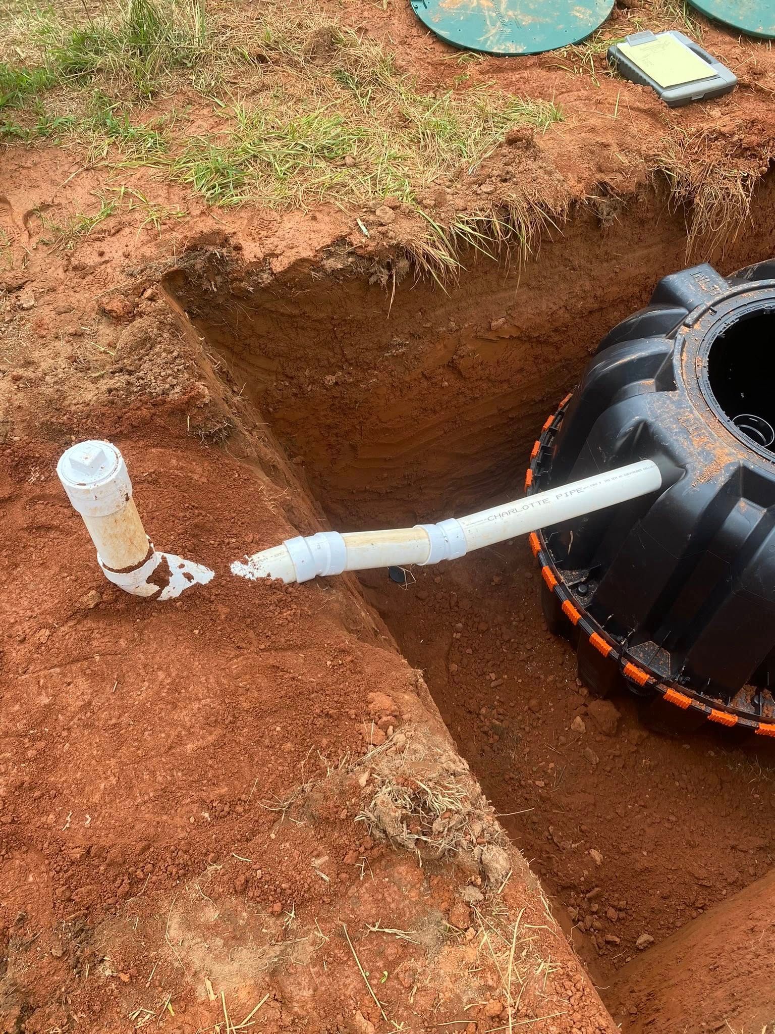 Septic tank installation in progress; white PVC pipes and red dirt visible.