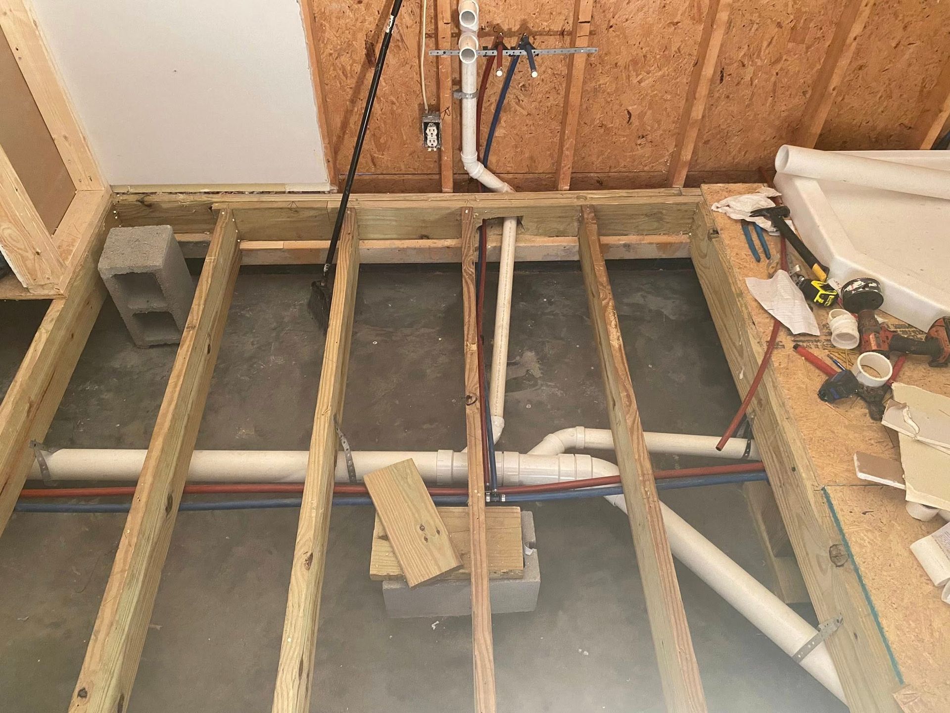Wooden floor joists, plumbing pipes, and concrete floor in a construction setting.